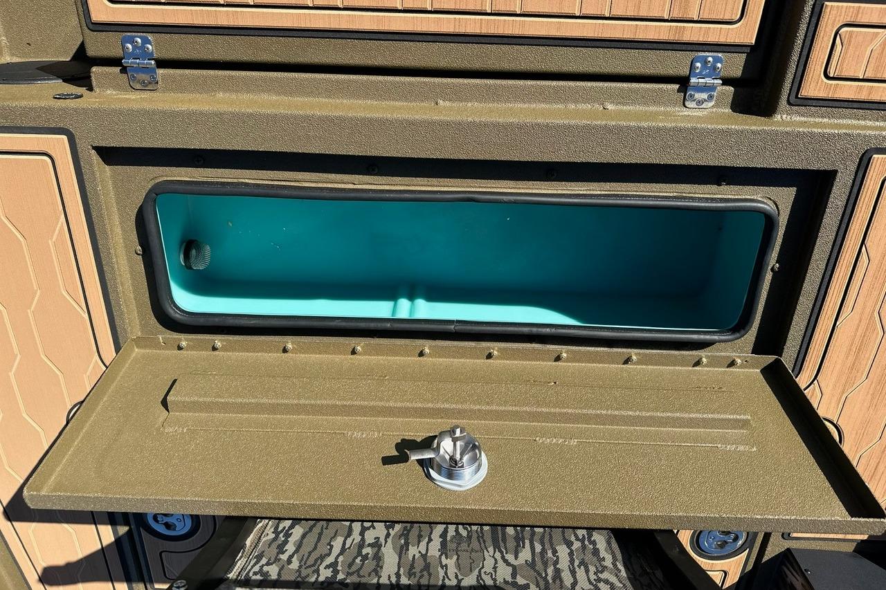 Open storage compartment in 2026 Avid 18 Commander boat, featuring teal interior and secure latch.