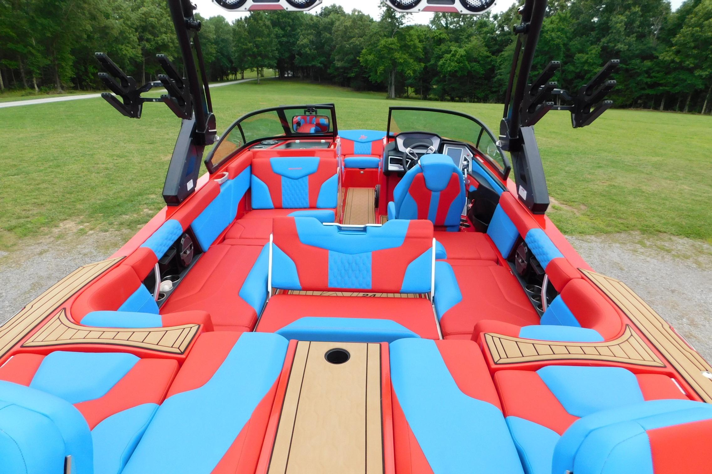 2022 MasterCraft NXT24 boat interior with vibrant red and blue seating, surrounded by lush greenery.