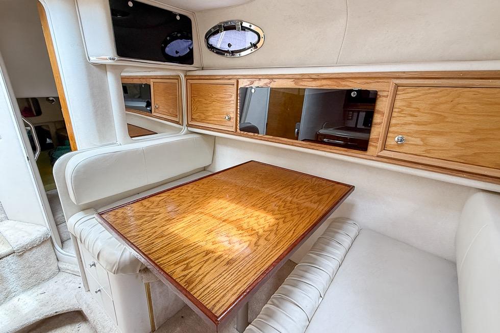 1999 Sea Ray 290 Sundancer cabin interior with wooden table and storage cabinets.