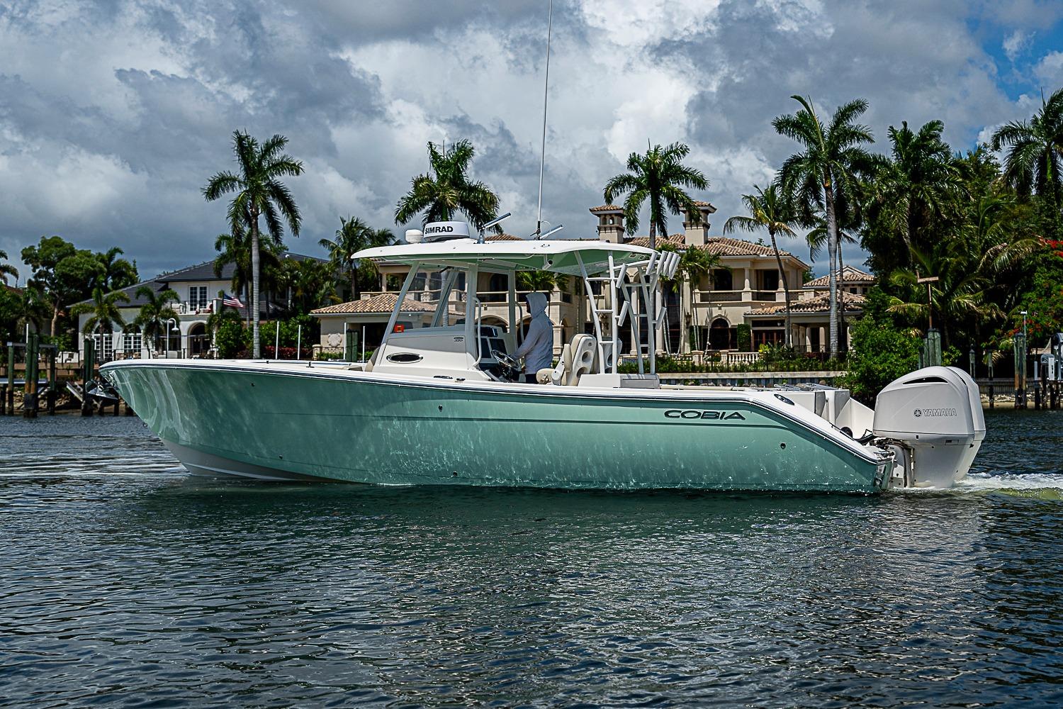 2019 Cobia 320 Center Console boat cruising on a scenic waterway with palm trees.
