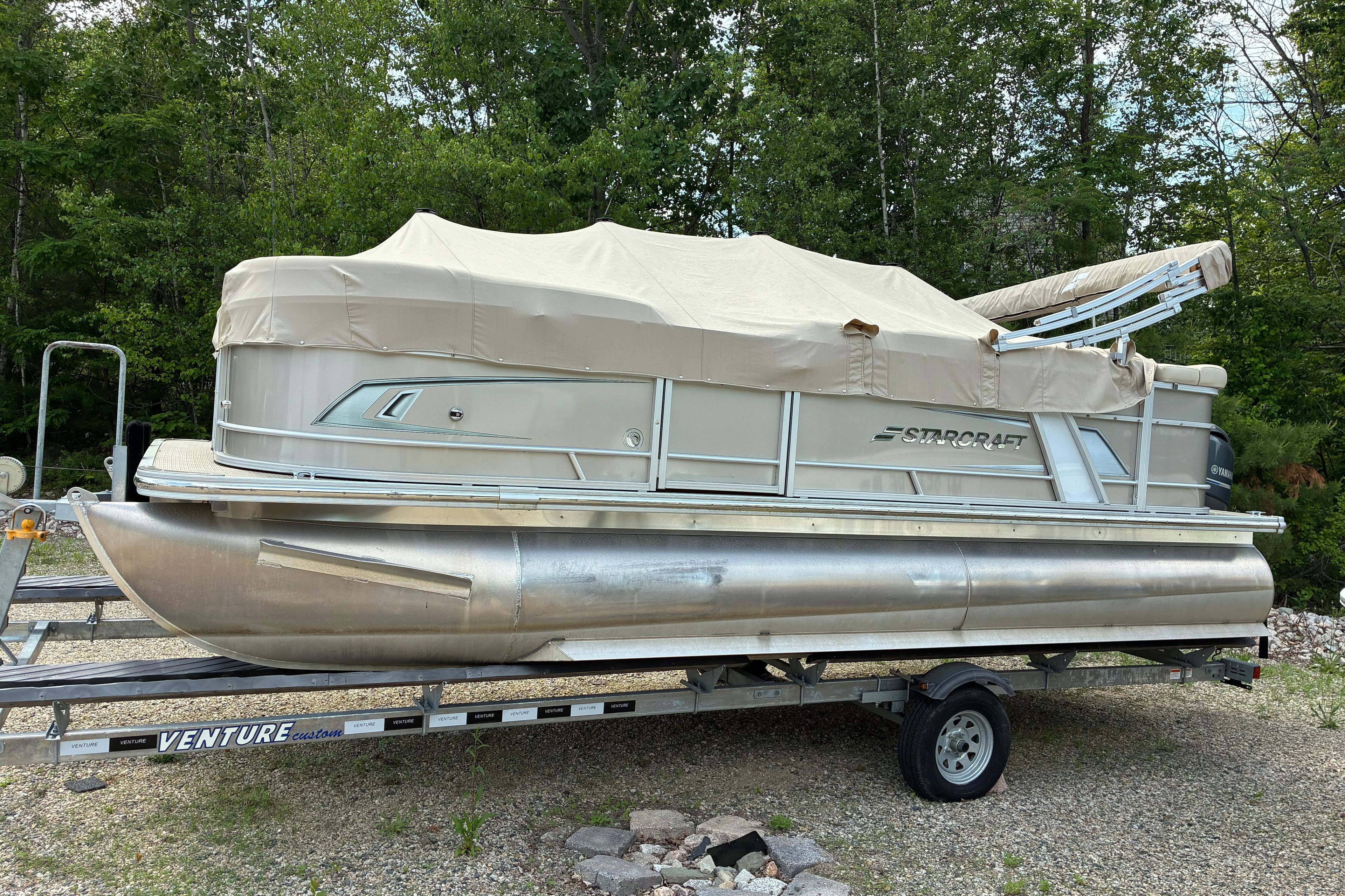2020 Starcraft EX 20 C pontoon boat on trailer, covered, surrounded by trees.