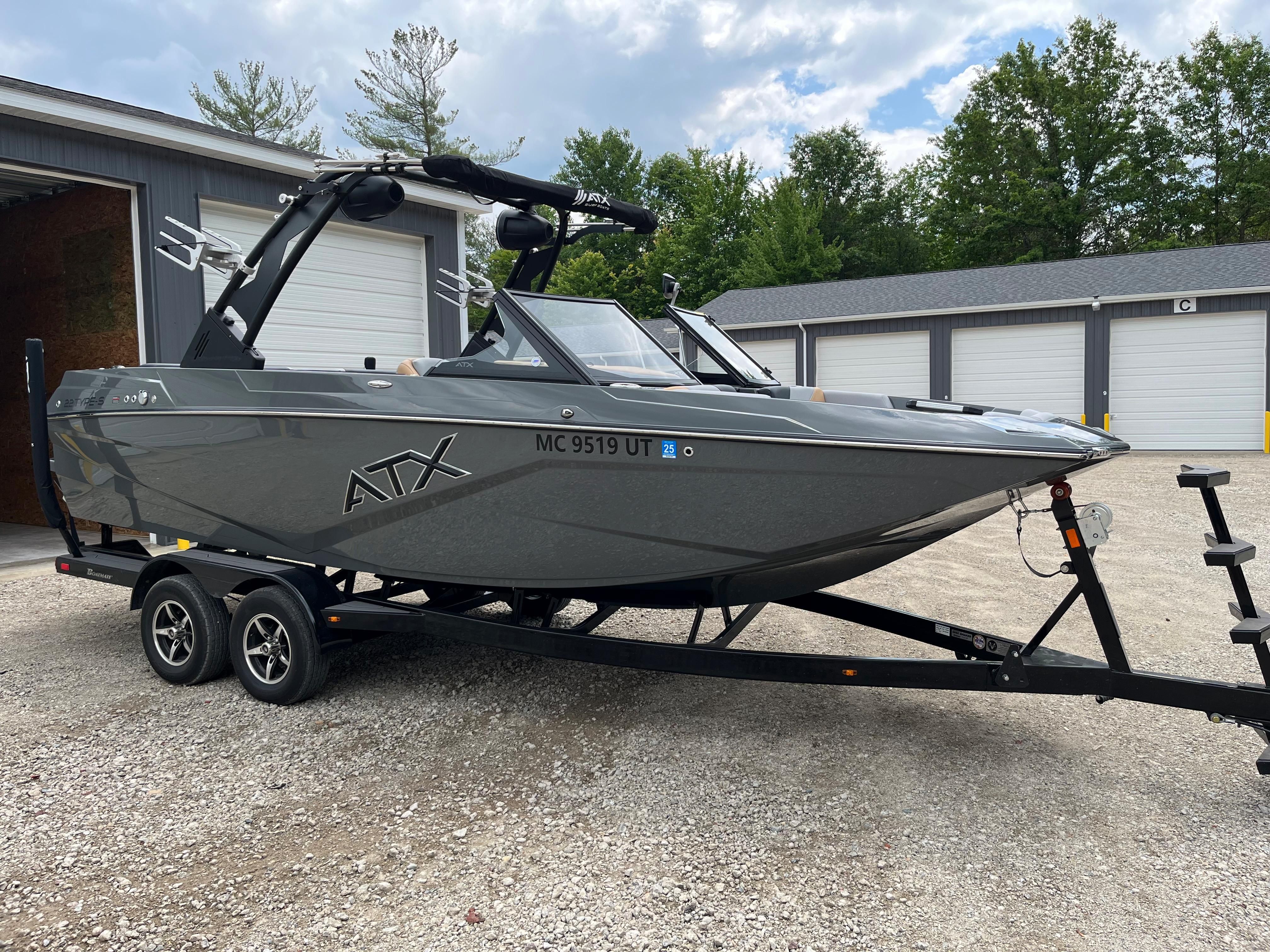 A gray 2022 ATX Surf Boat 22 Type-S on a trailer in front of garages.