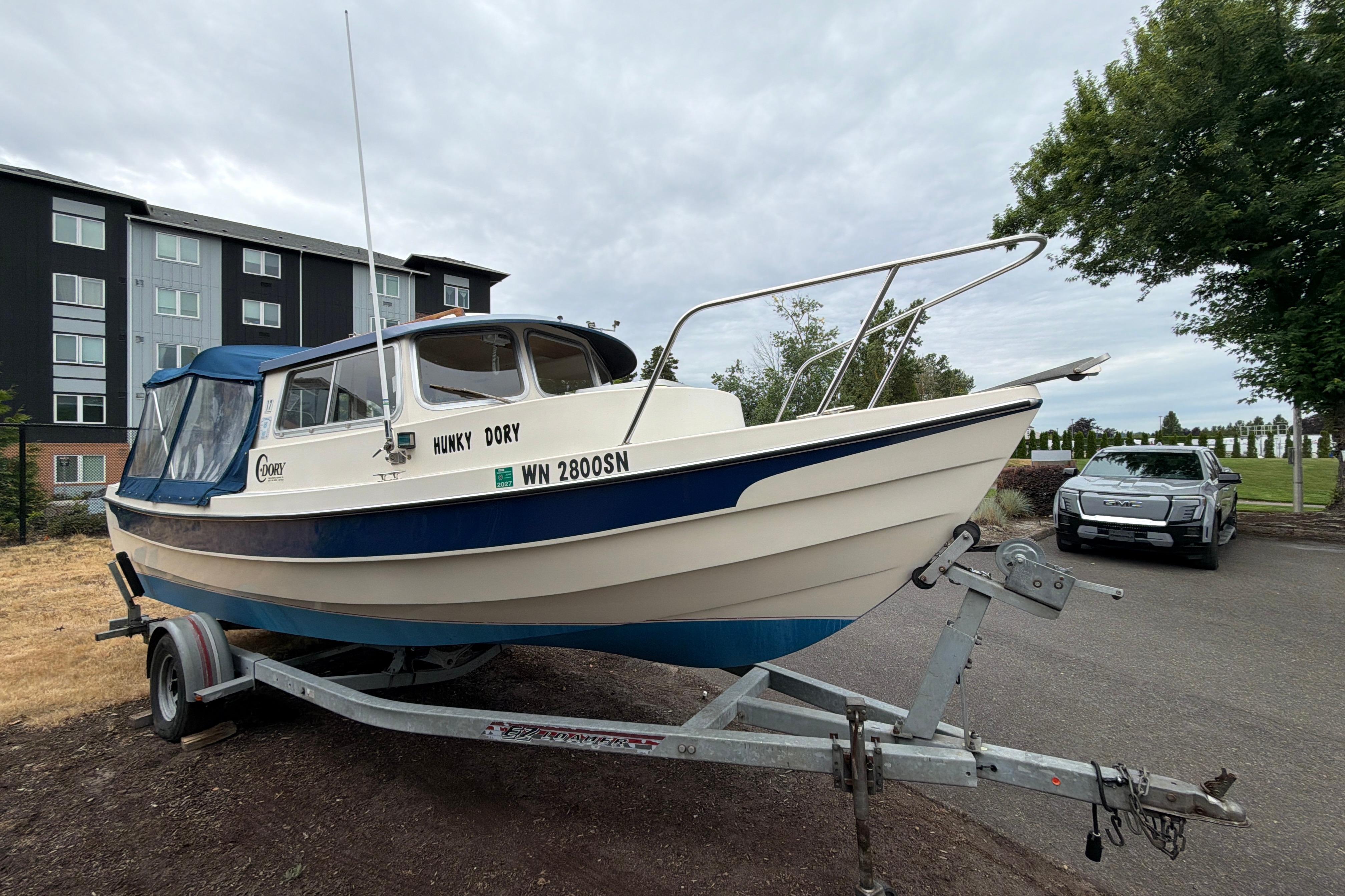 1989 C-Dory 22' Angler boat on trailer, parked near a building and a GMC vehicle.