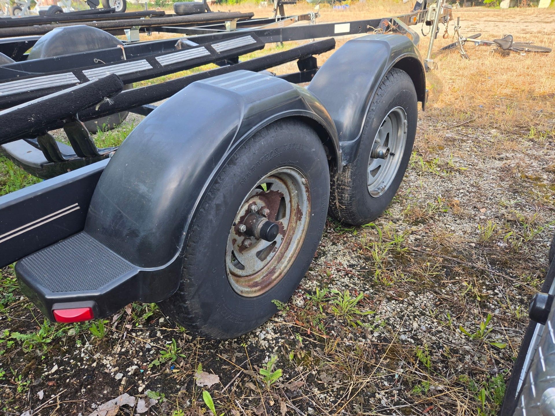 A boat trailer with two large wheels on a gravel surface.