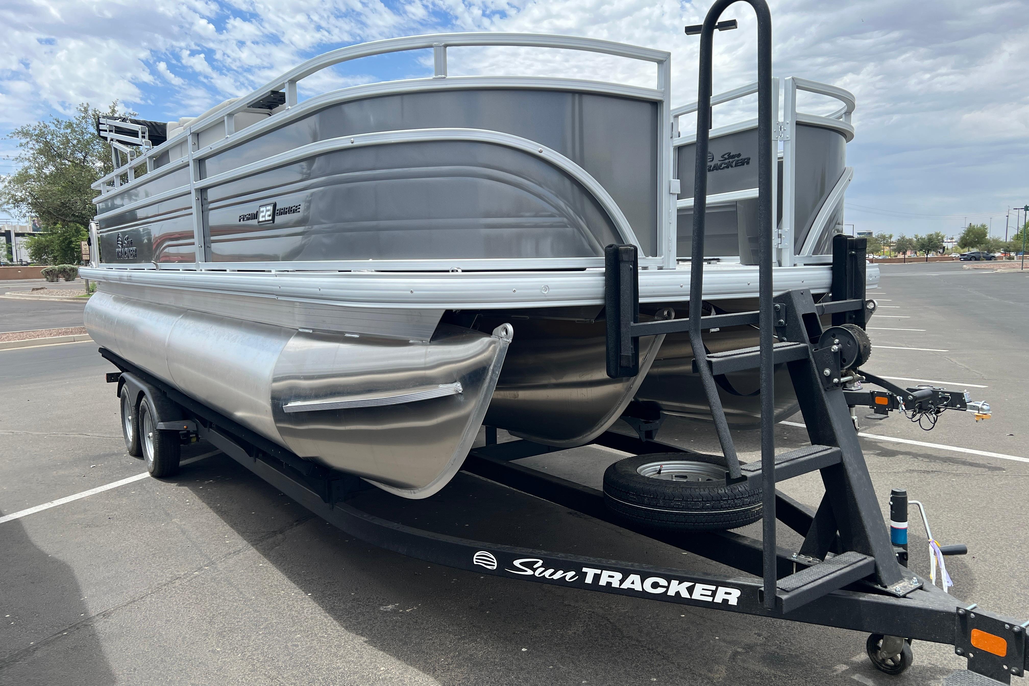 2026 Sun Tracker Fishin' Barge 22 XP3 pontoon boat on trailer in parking lot.