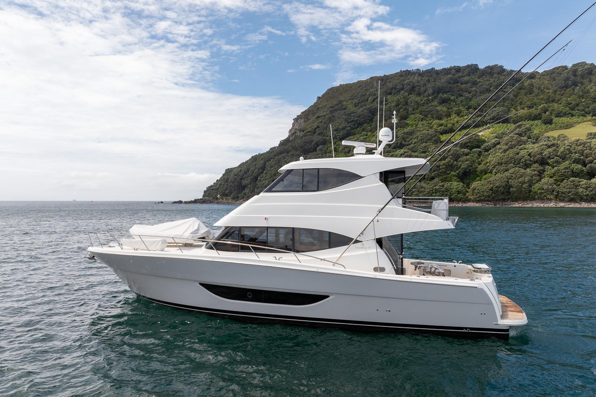 2021 Maritimo M51 yacht cruising near a lush, green coastline under a partly cloudy sky.