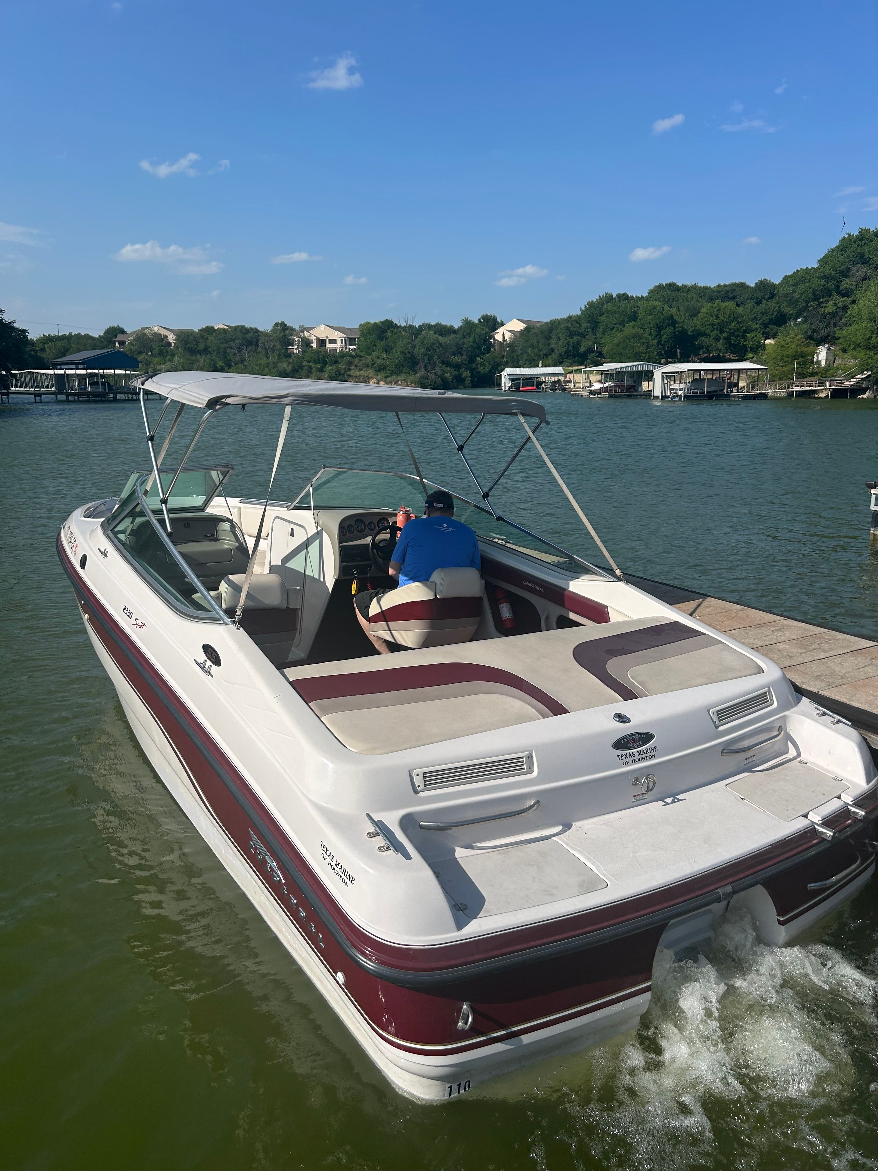 A 1995 Chaparral 2330 boat on a calm lake with a driver under a sunshade.