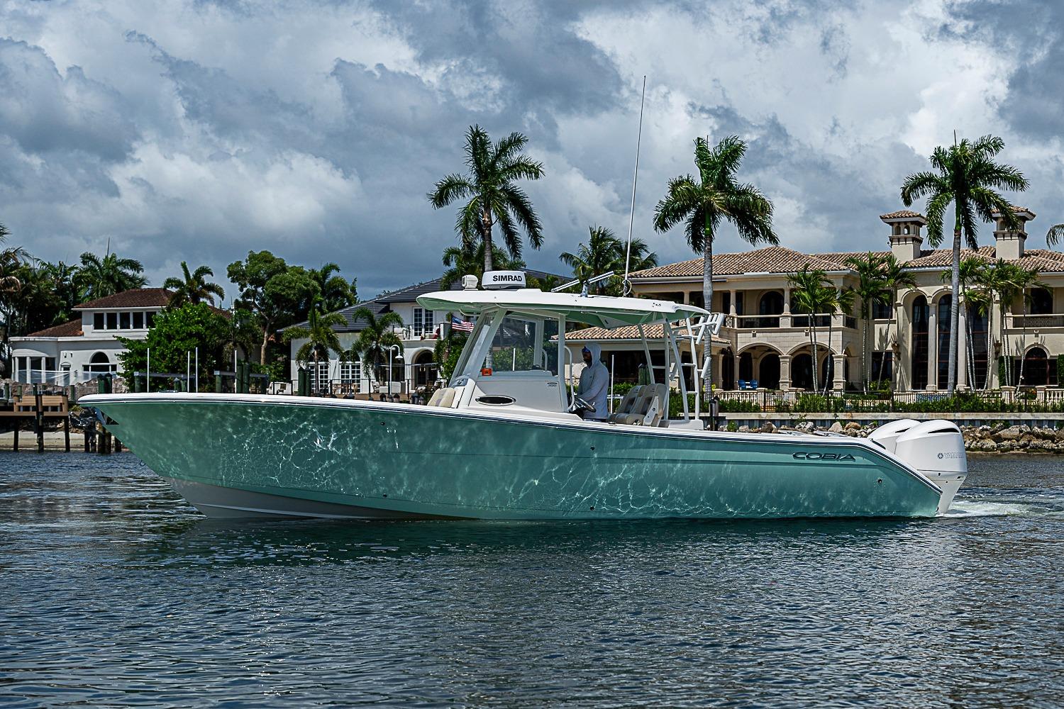2019 Cobia 320 Center Console boat cruising near luxury waterfront homes.