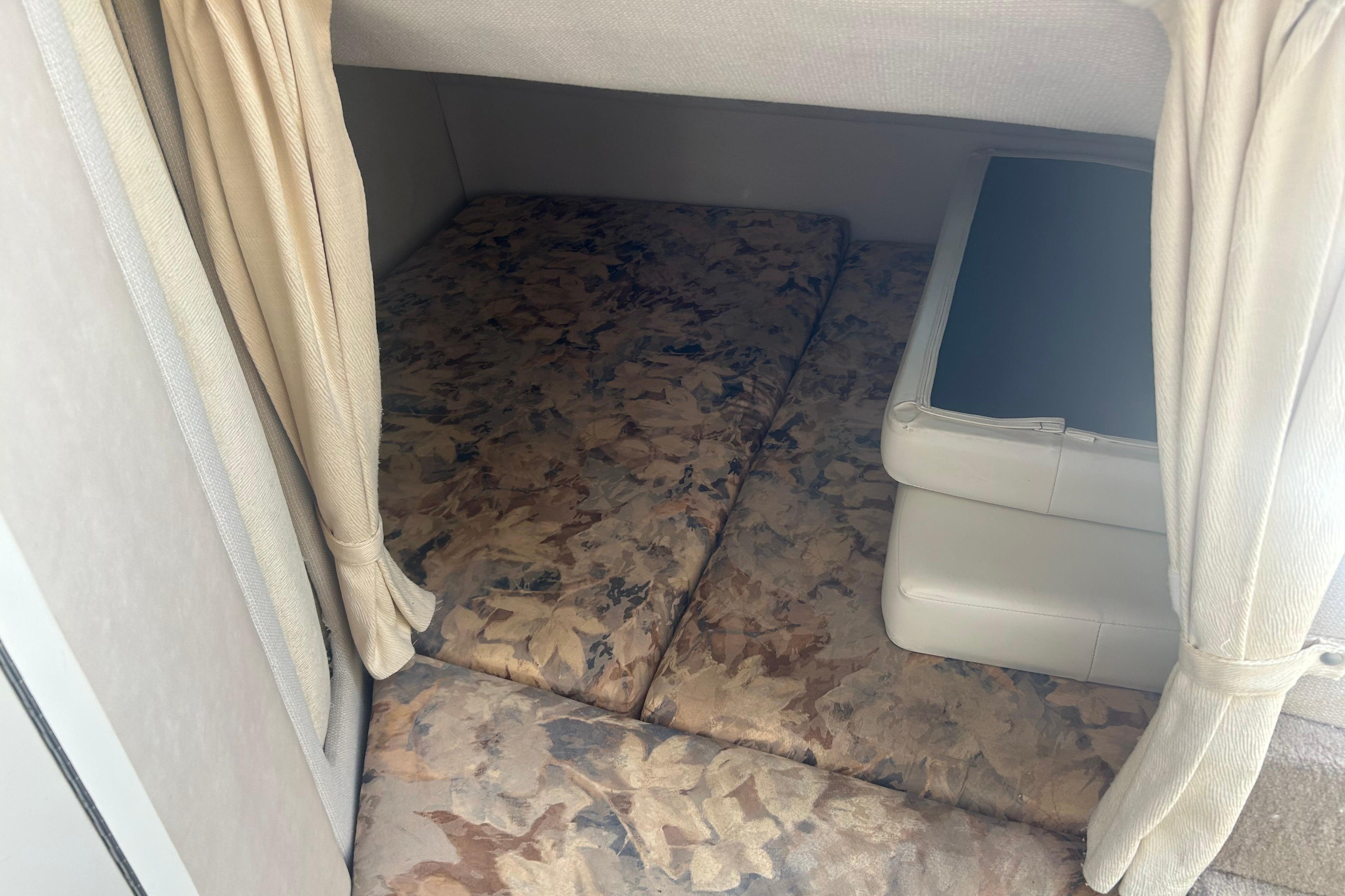 1998 Four Winns 258 Vista cabin interior with patterned cushions and beige curtains.