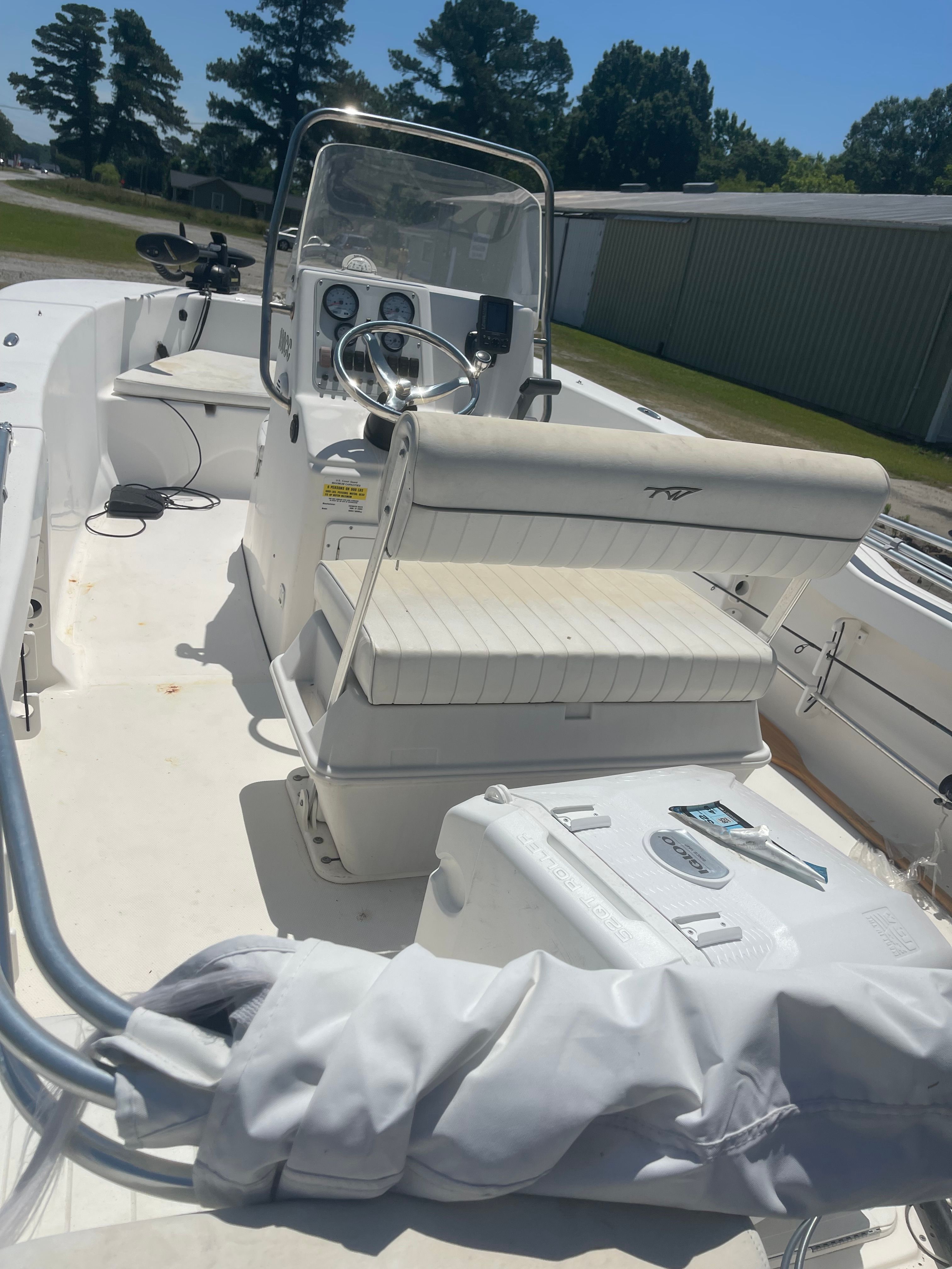 A white boat with a steering console and bench seat, parked on dry land.