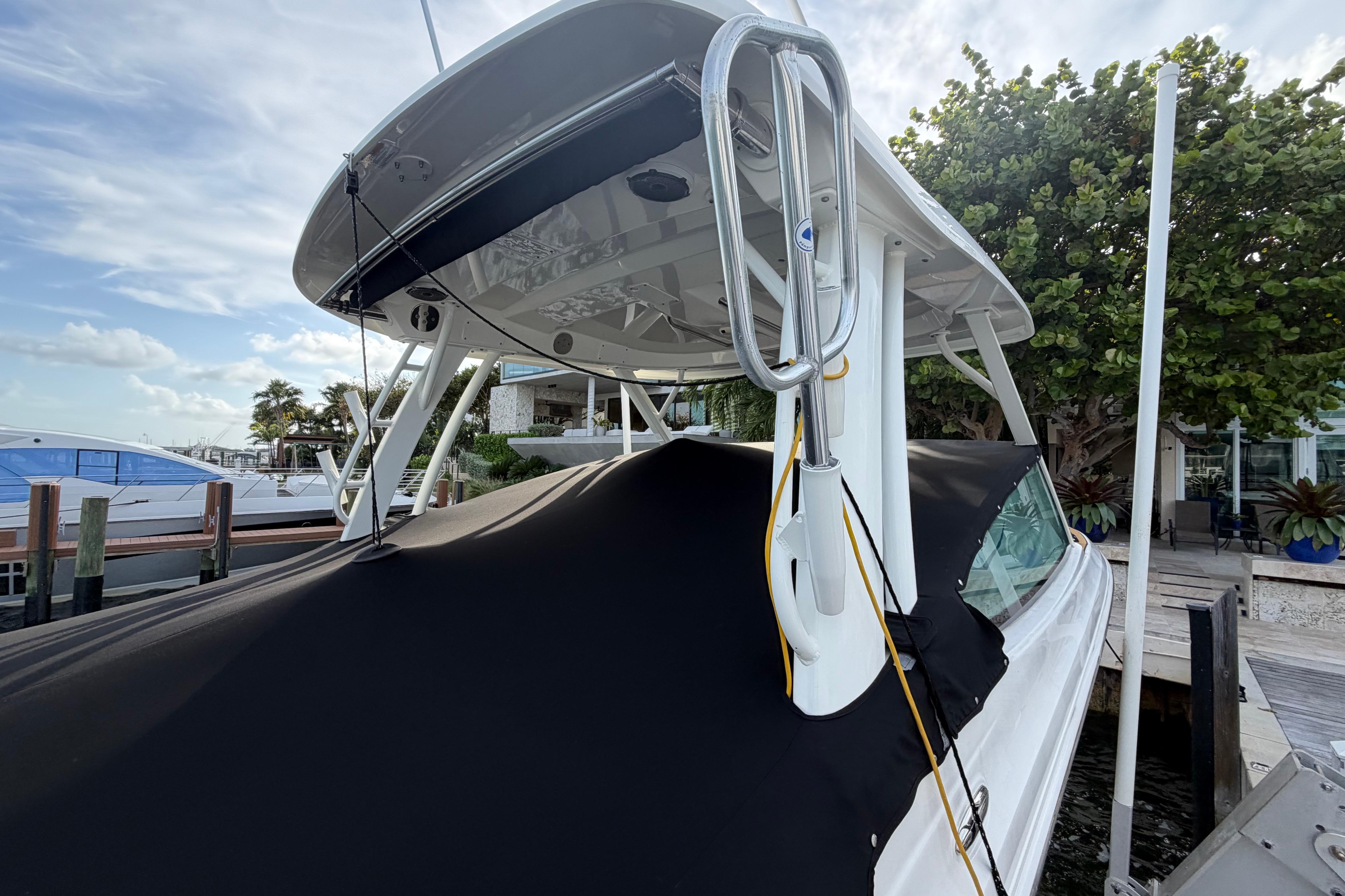 2022 Boston Whaler 280 Vantage boat docked, covered with black tarp, surrounded by trees.