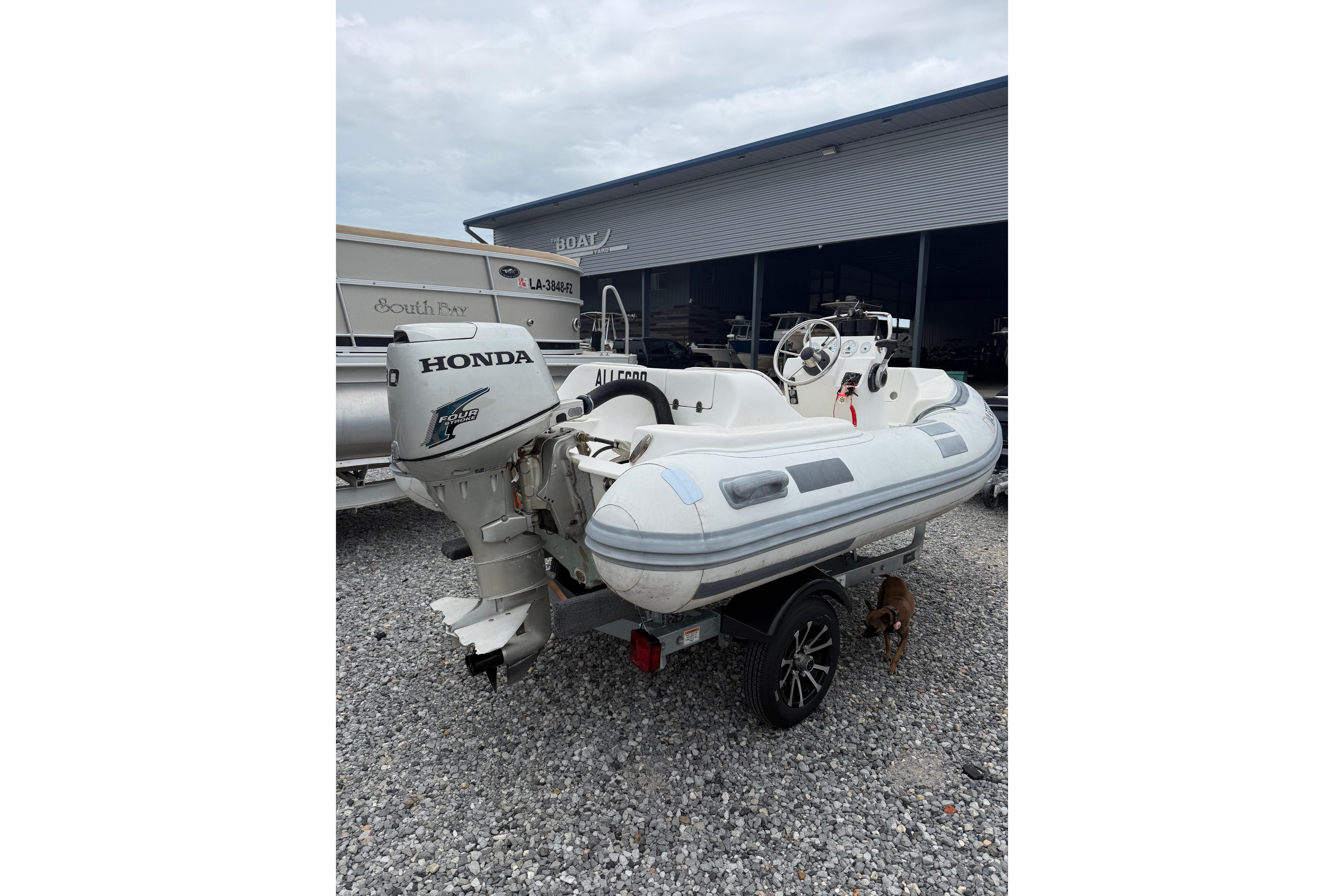 Inflatable boat with Honda outboard motor, parked on gravel near a building.