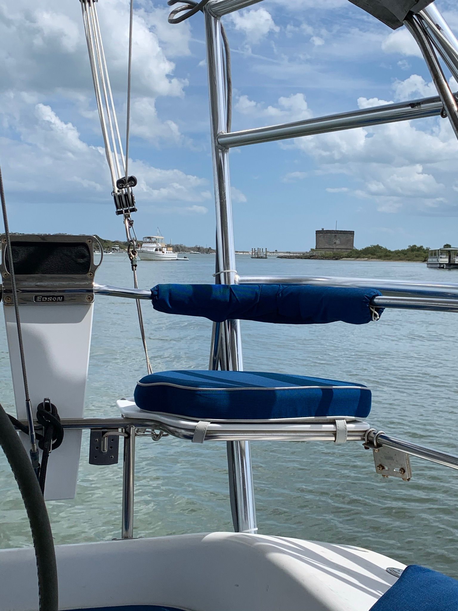 A sailboat with blue cushions on calm water under a cloudy sky.