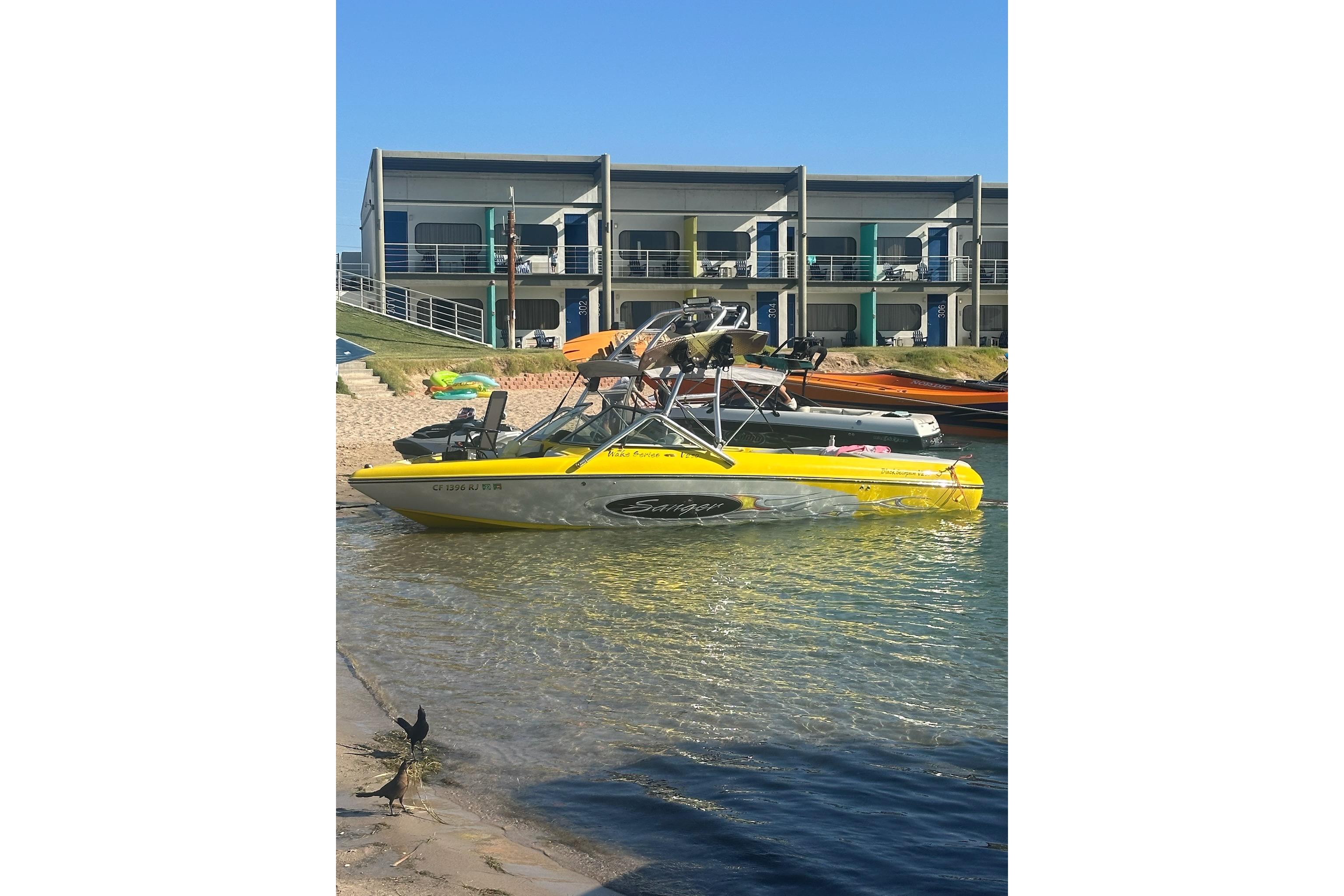 Yellow 2006 Sanger V230 boat docked by a modern waterfront building.