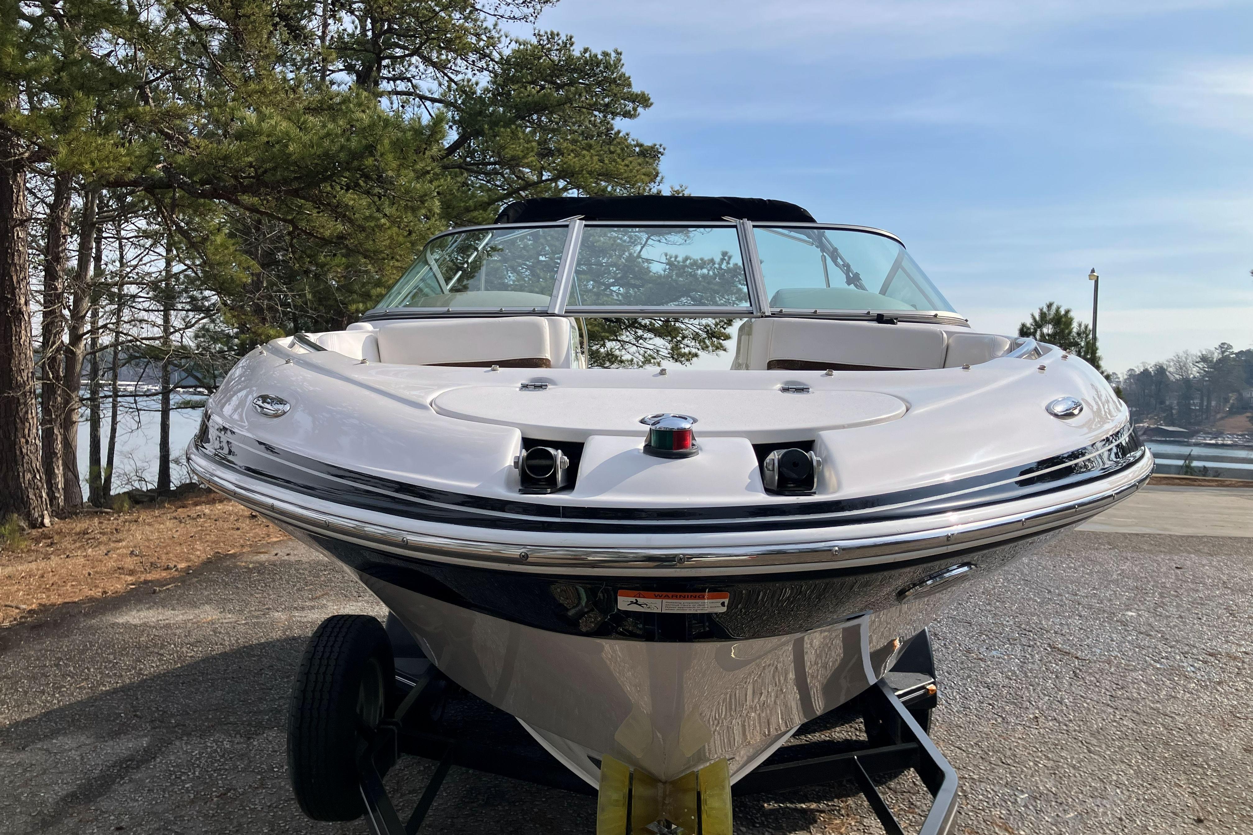 2006 Four Winns 240 Horizon boat on trailer, surrounded by trees and lake view.