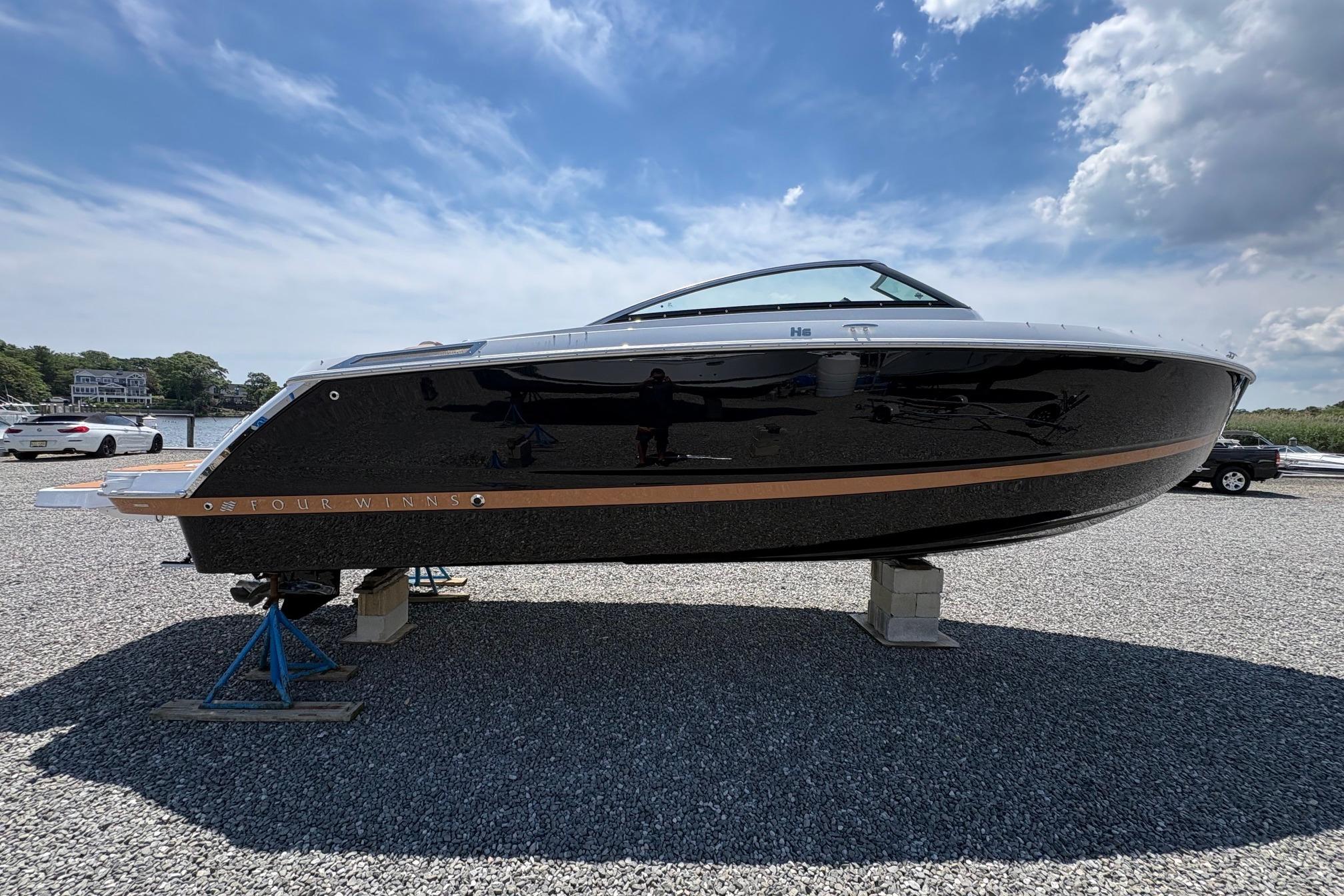 2026 Four Winns H6 boat displayed on gravel lot under blue sky.