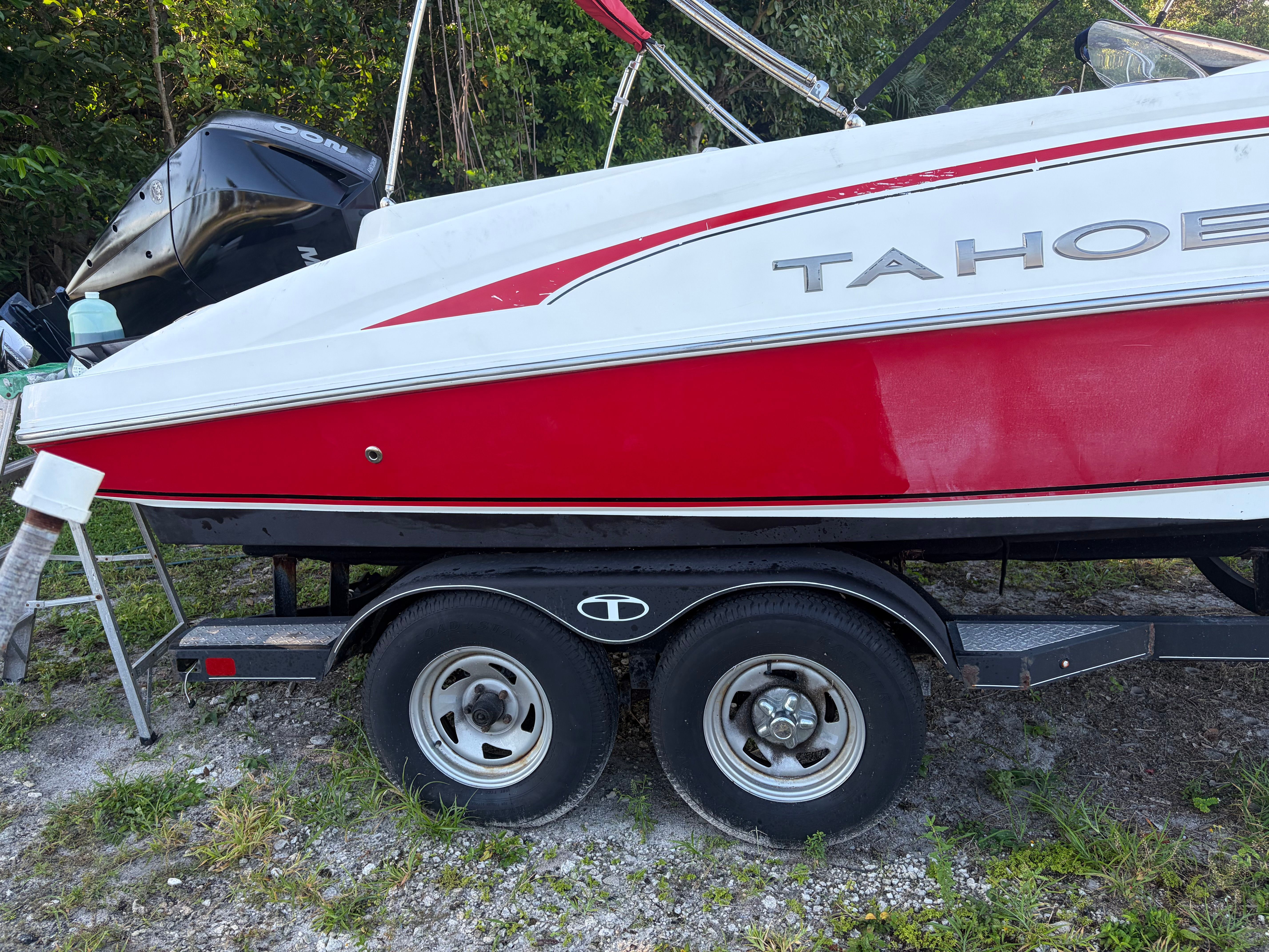 A red and white Tahoe boat on a trailer, surrounded by trees.