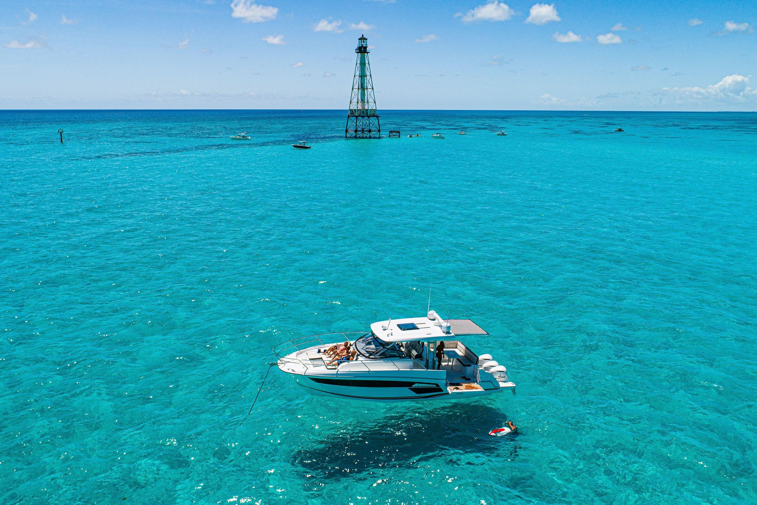 2026 Jeanneau Leader 12.5 WA yacht in clear turquoise waters near a lighthouse.