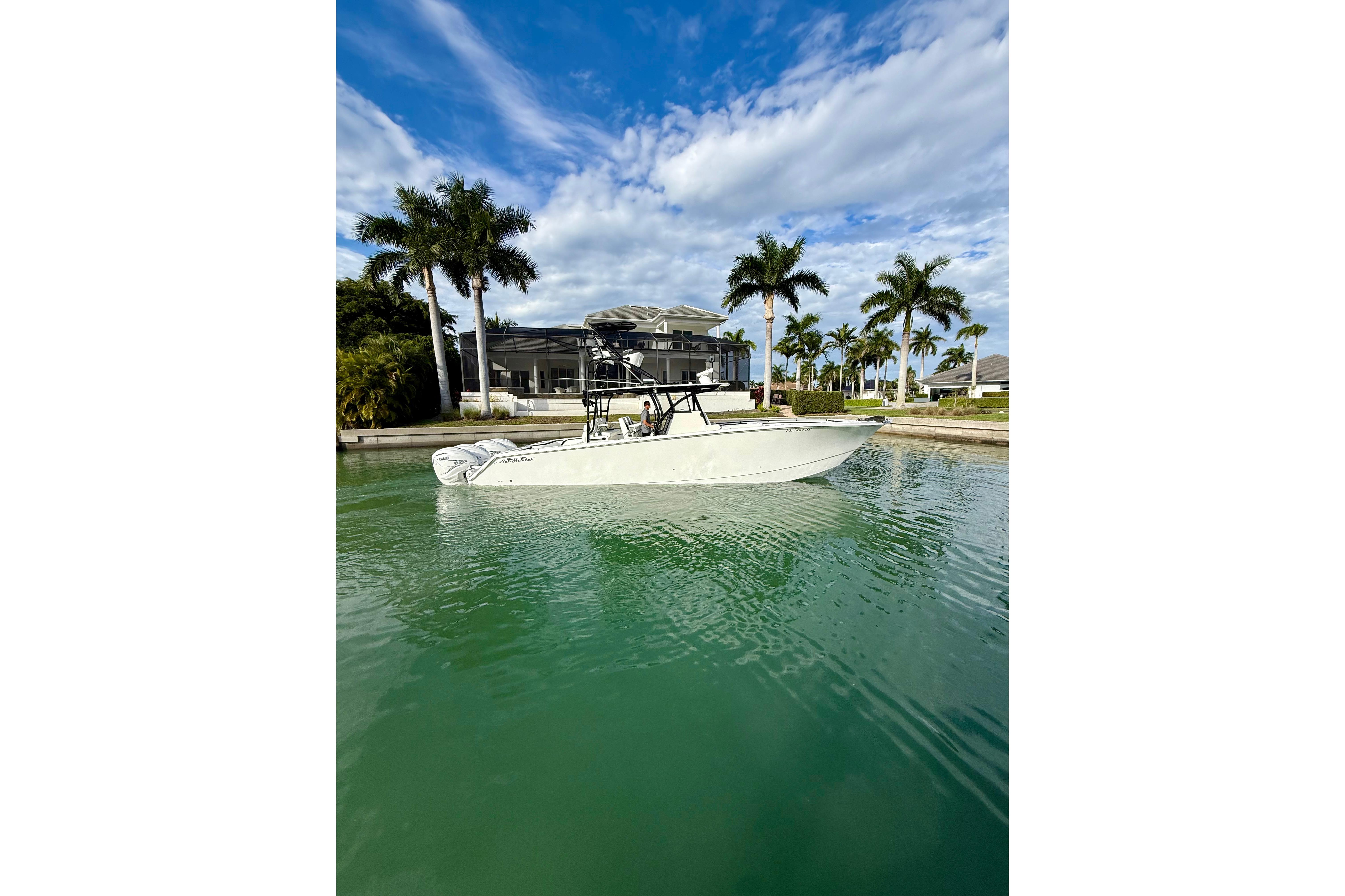2020 SeaHunter 41 CTS boat on calm water, surrounded by palm trees and a modern house.