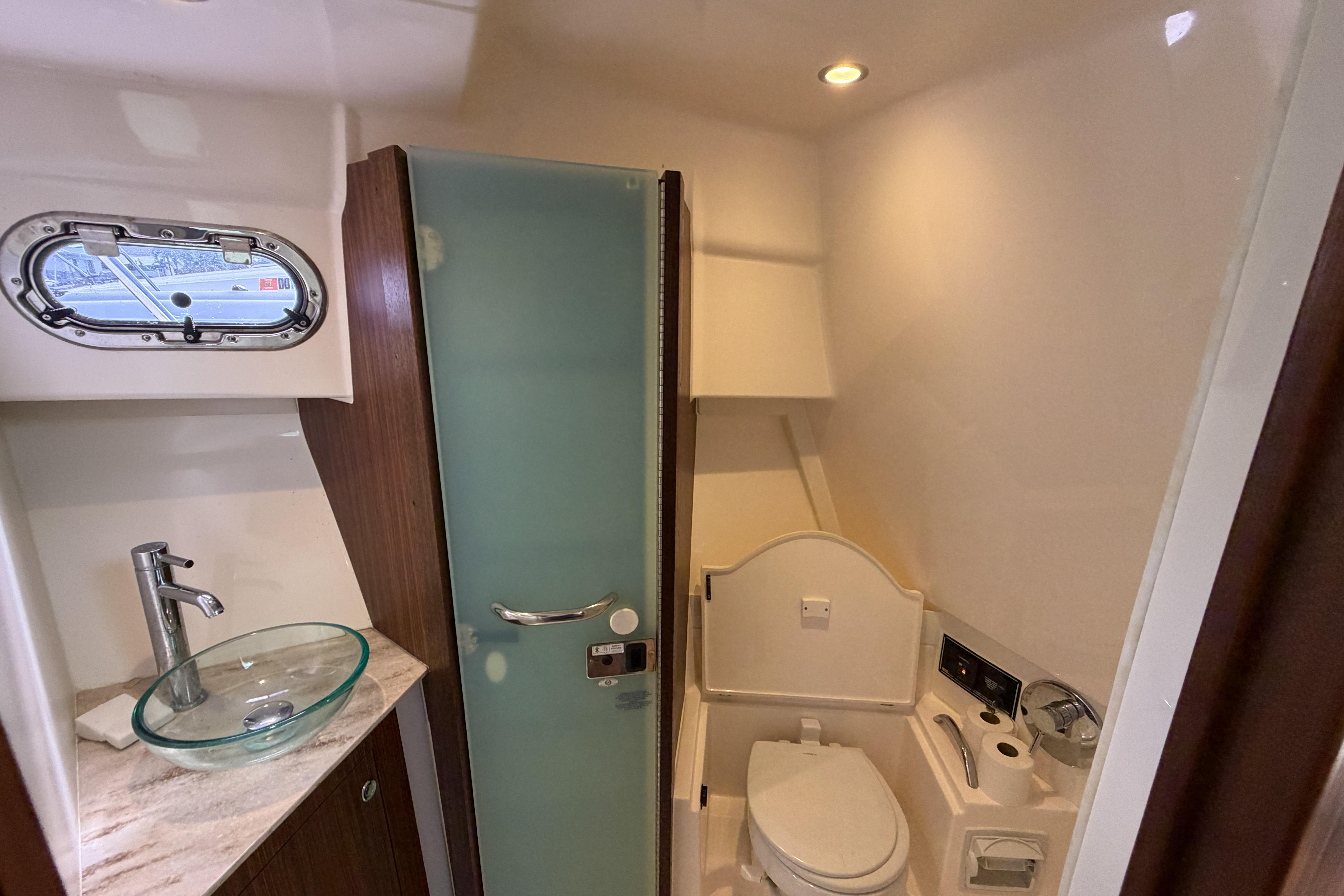 2018 Pursuit OS 355 Offshore bathroom with glass sink, toilet, and frosted glass door.