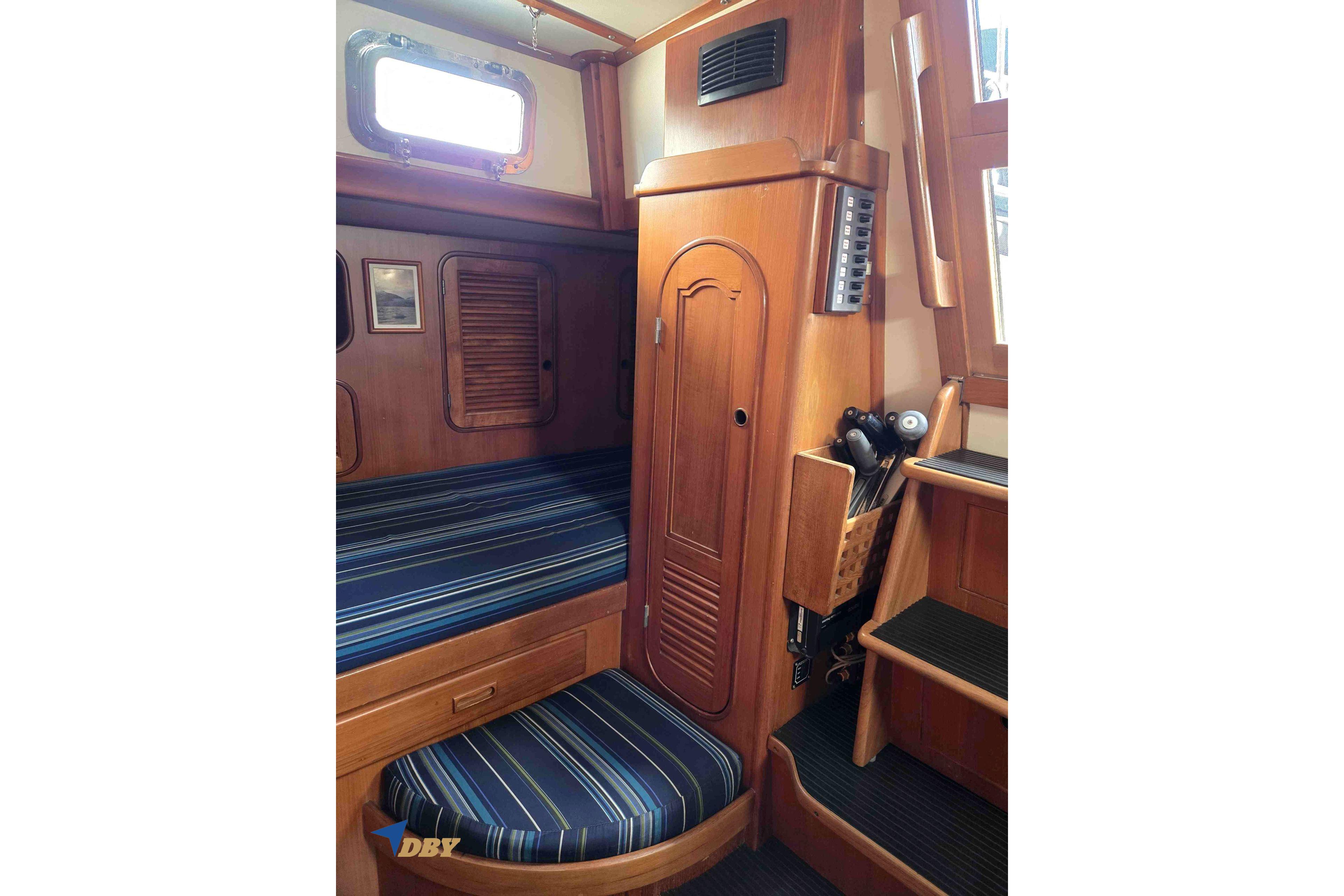 Cozy cabin interior of 1983 Mason 53 sailboat with wooden furnishings and striped cushions.