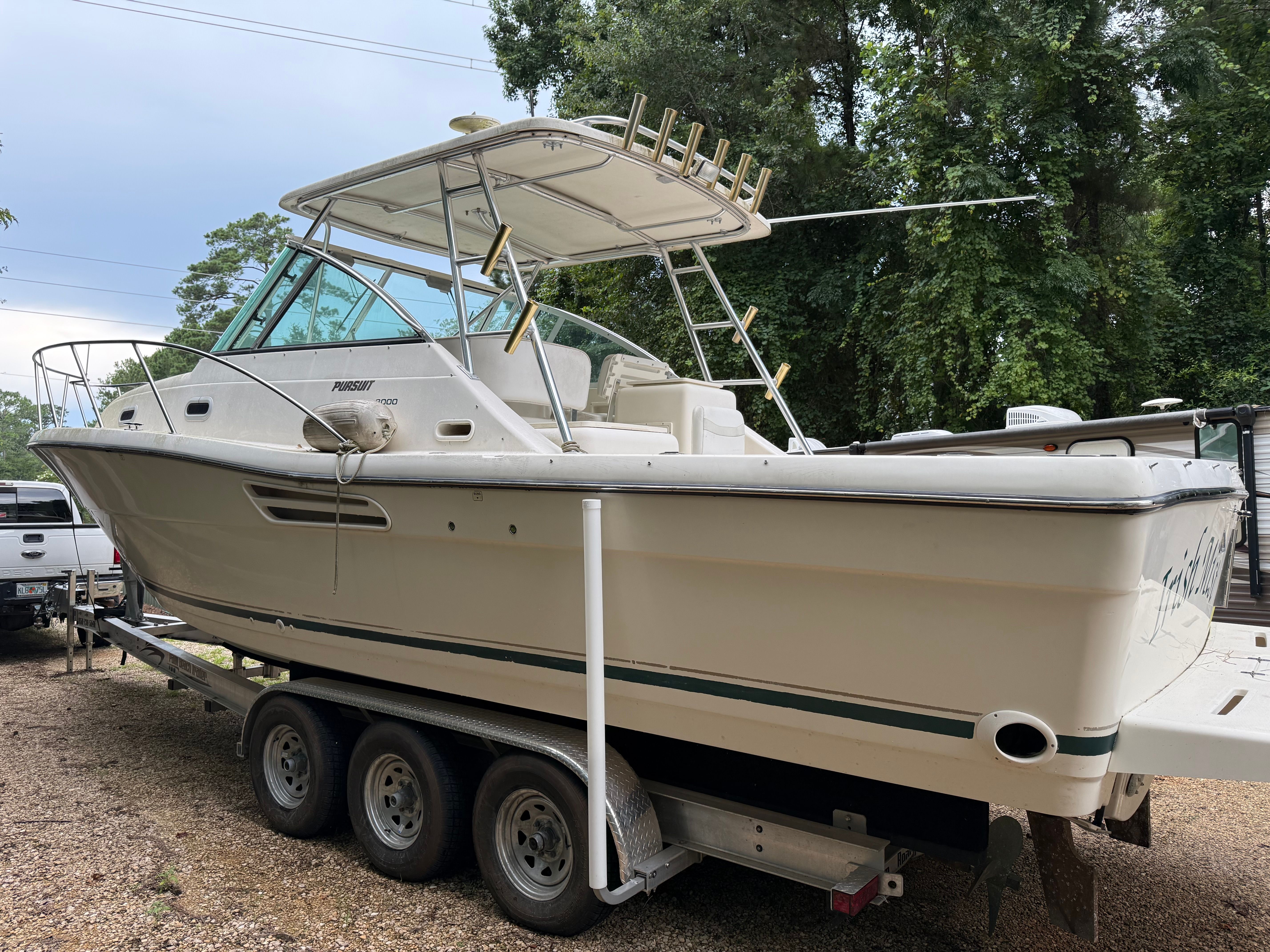 A 2002 Pursuit 3000 Express boat on a trailer, surrounded by trees.