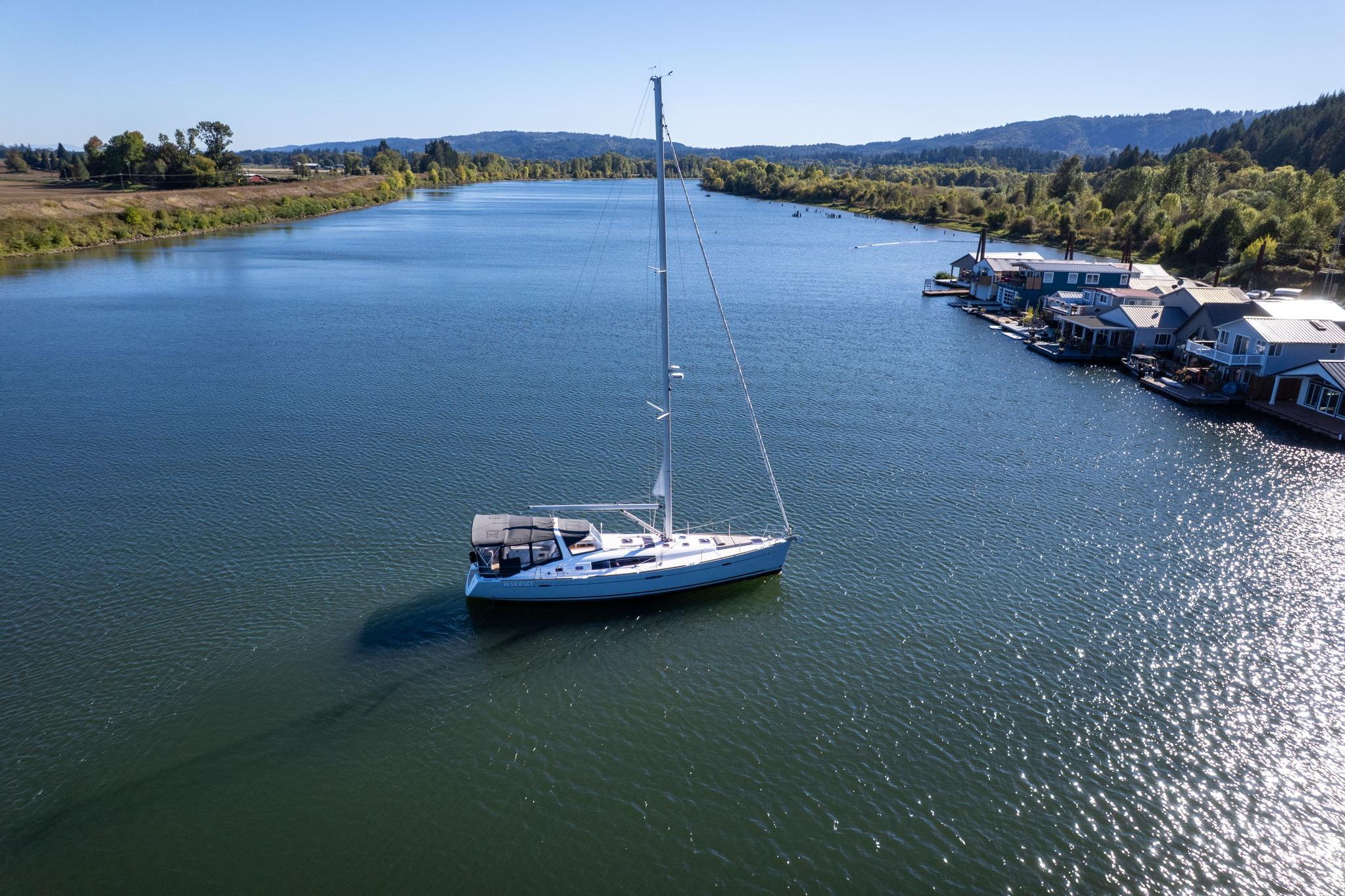 Beneteau Oceanis 50 sailboat on a serene river, surrounded by lush greenery and floating homes.