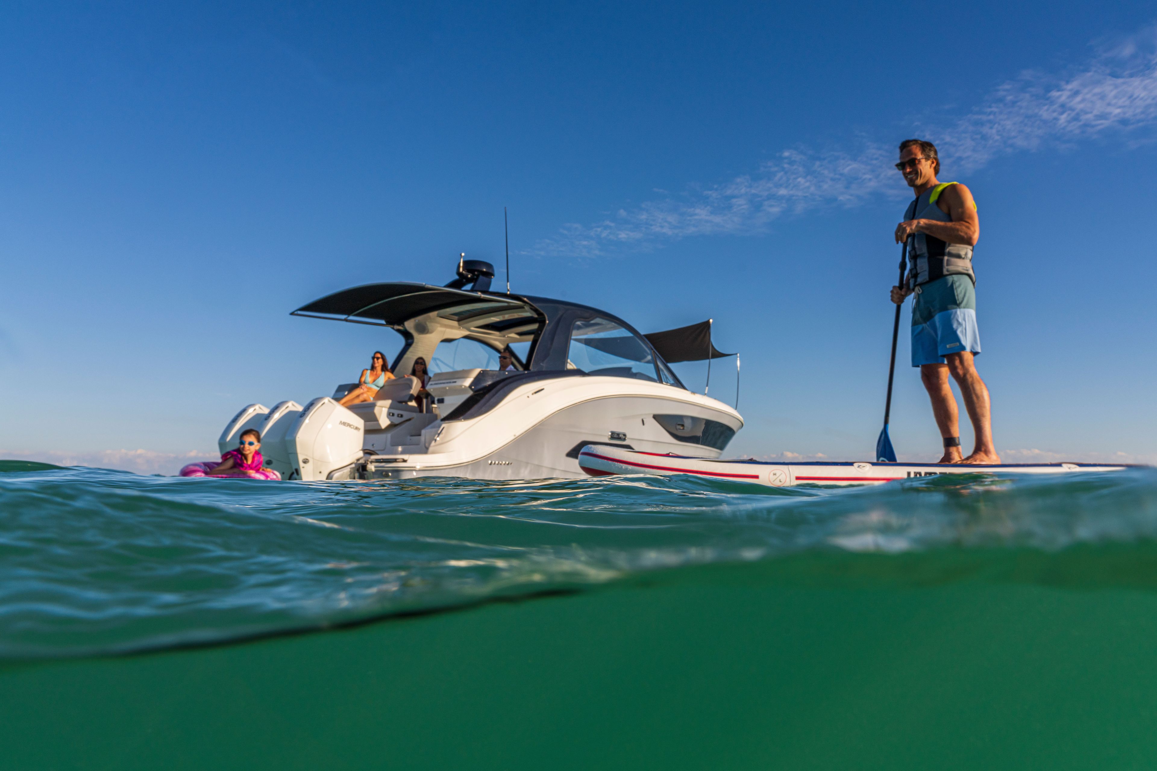 A man stands on a paddleboard next to a Sea Ray Sundancer 370 Outboard in the water.