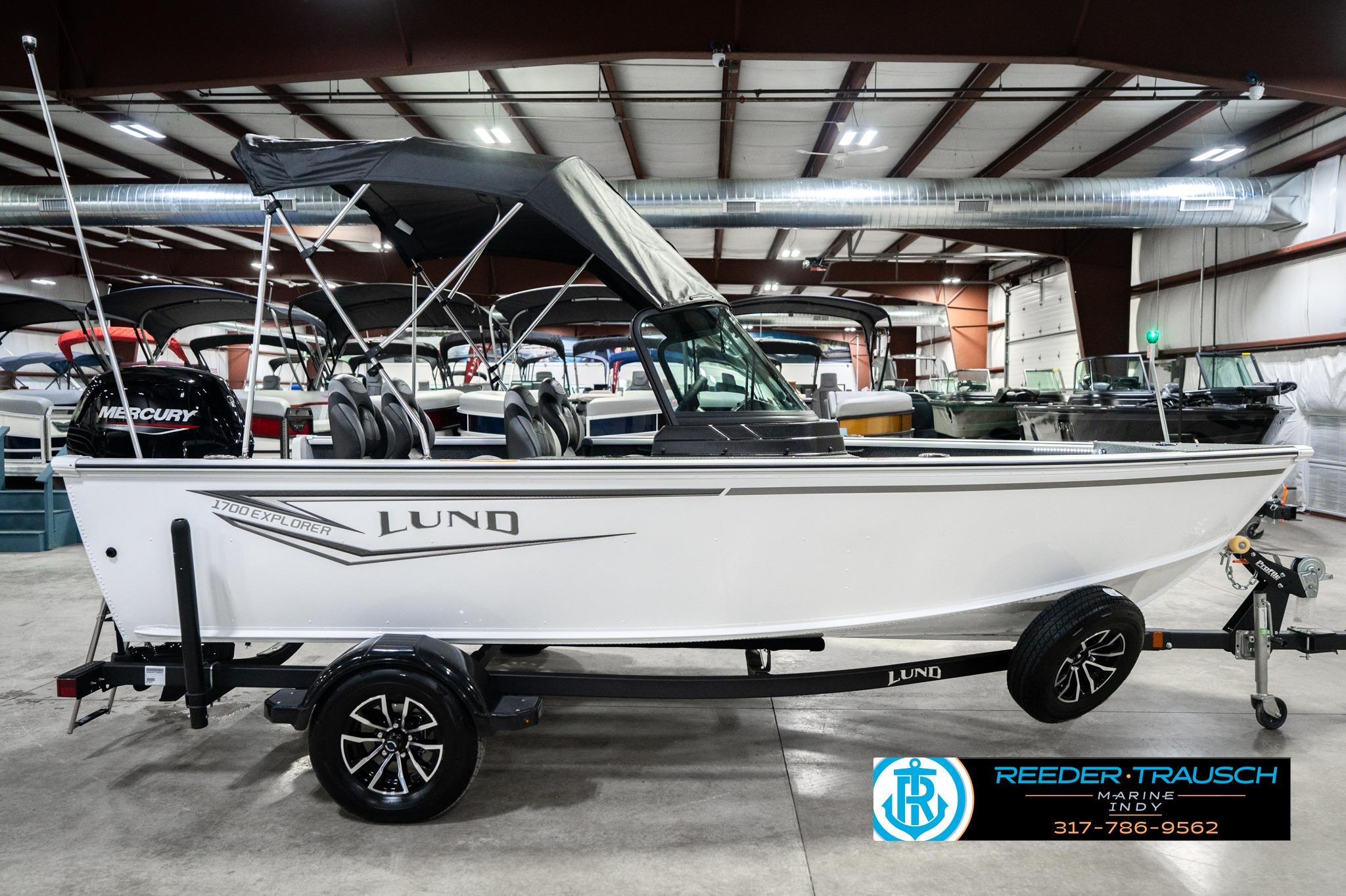 2026 Lund 1700 Explorer Sport boat in showroom, side view with trailer and Mercury engine.