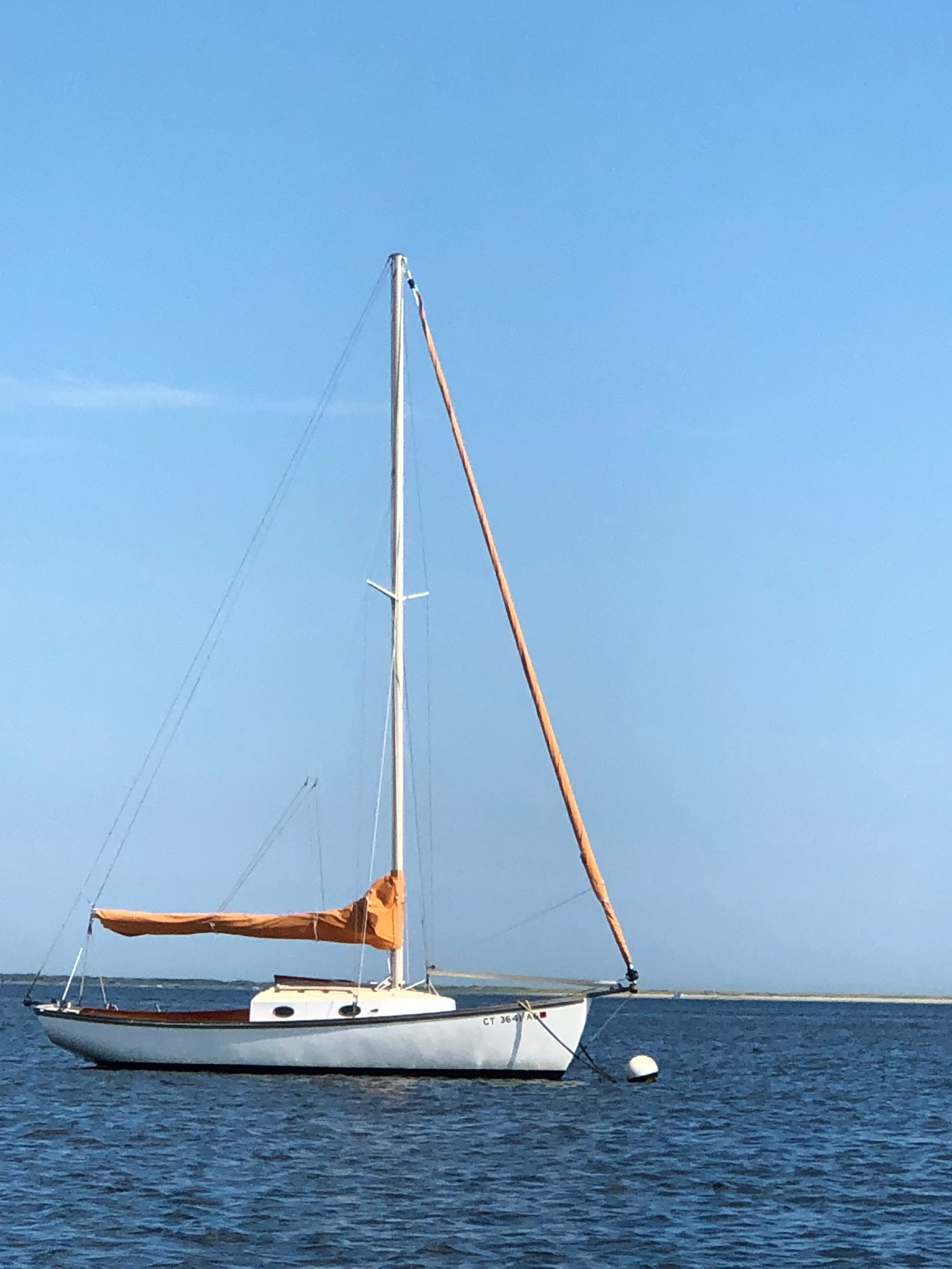 A 1973 Talman Yacht Menemsha-24 sails on calm water with an orange sail.