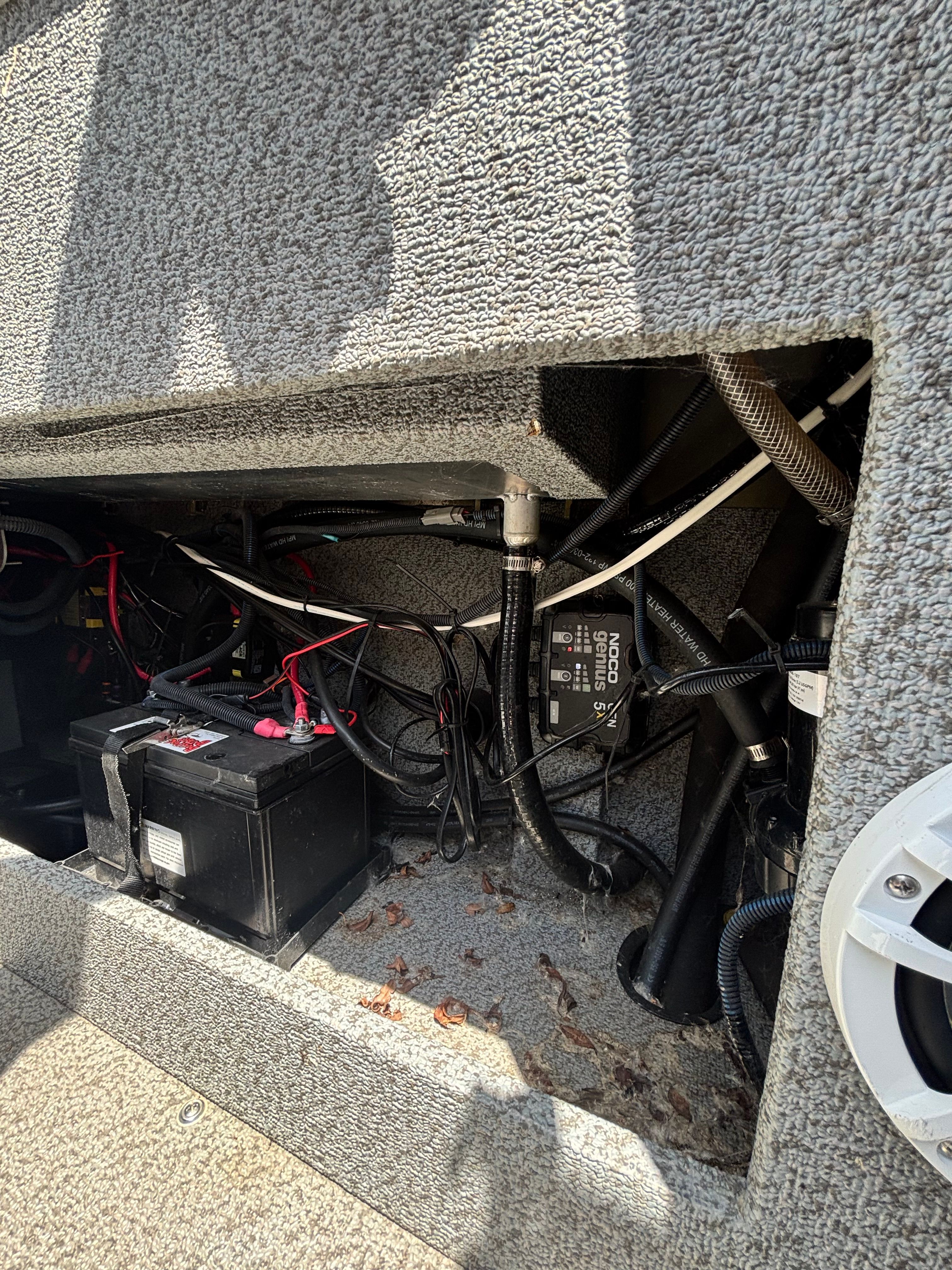 An open compartment with a battery and wires inside a boat.