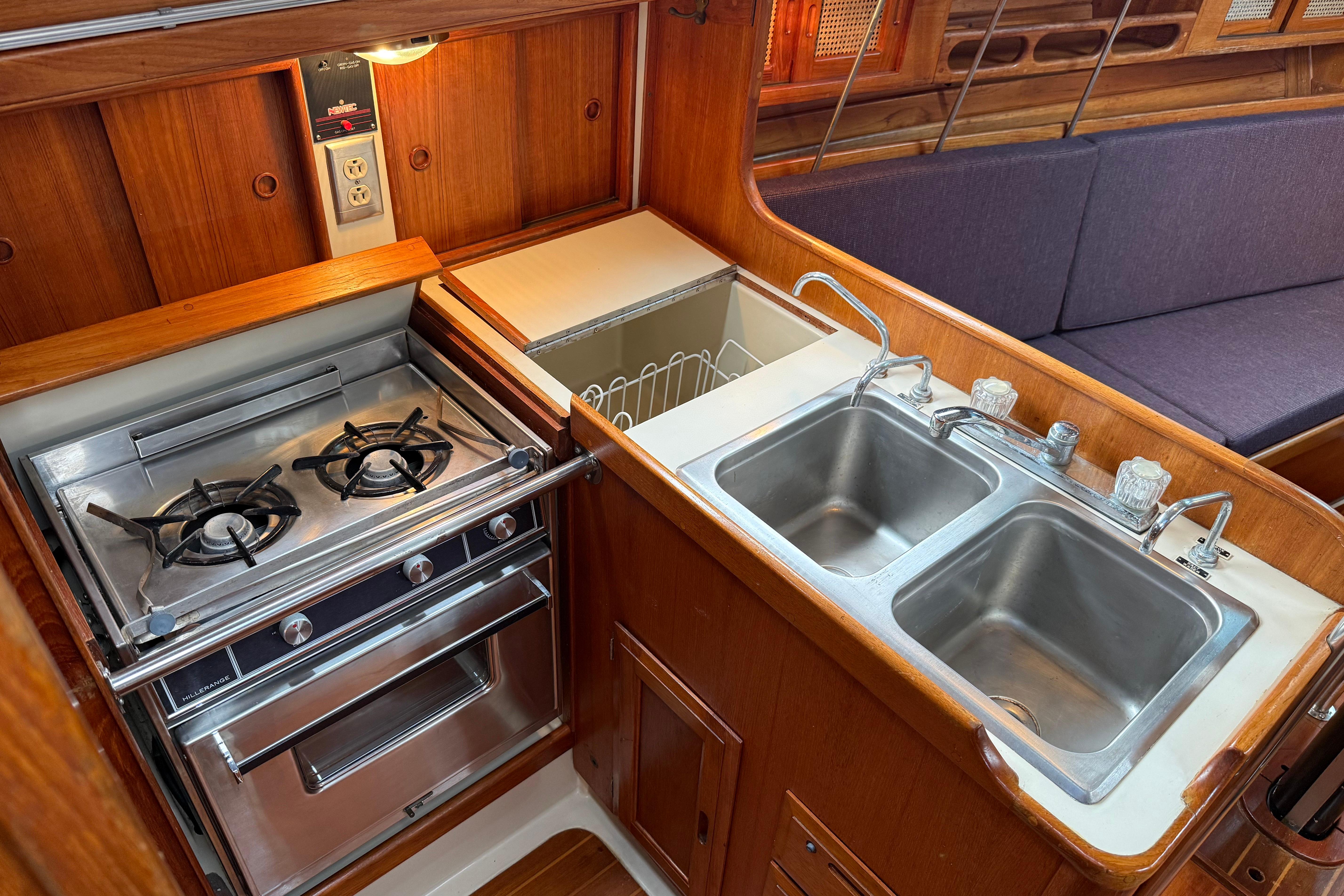 Compact galley kitchen in 1988 Ericson 32-200 sailboat with stove, double sink, and wood cabinetry.