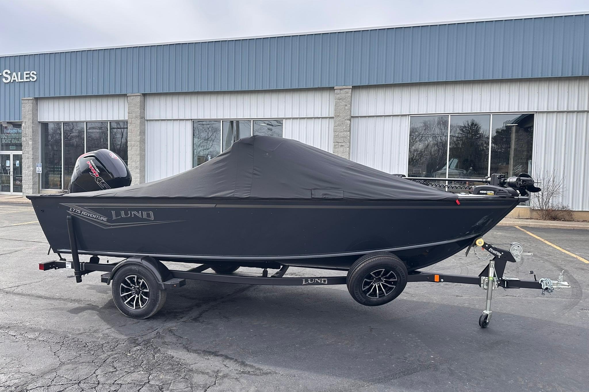 2026 Lund 1775 Adventure Sport boat with cover on trailer, parked outside a sales building.