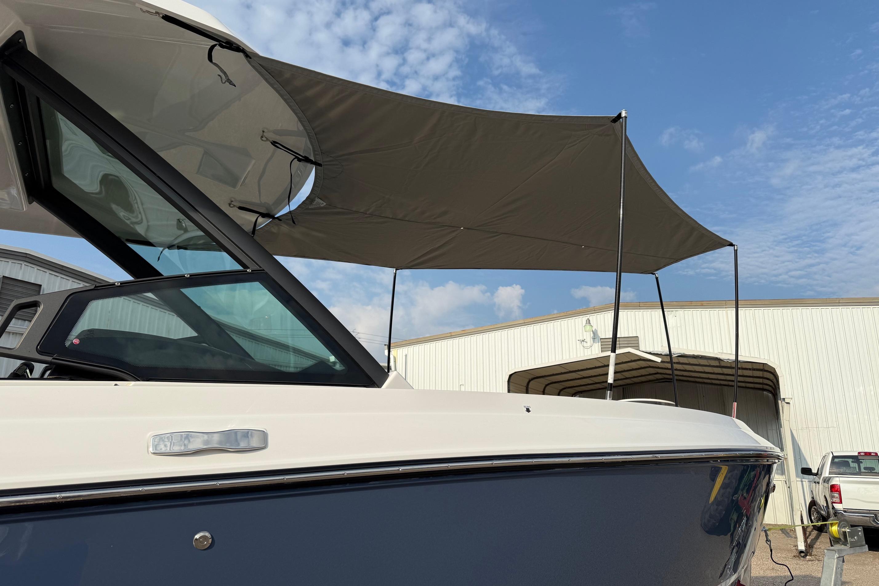 2026 Monterey Elite 25 OB boat with canopy, parked near a warehouse under a blue sky.