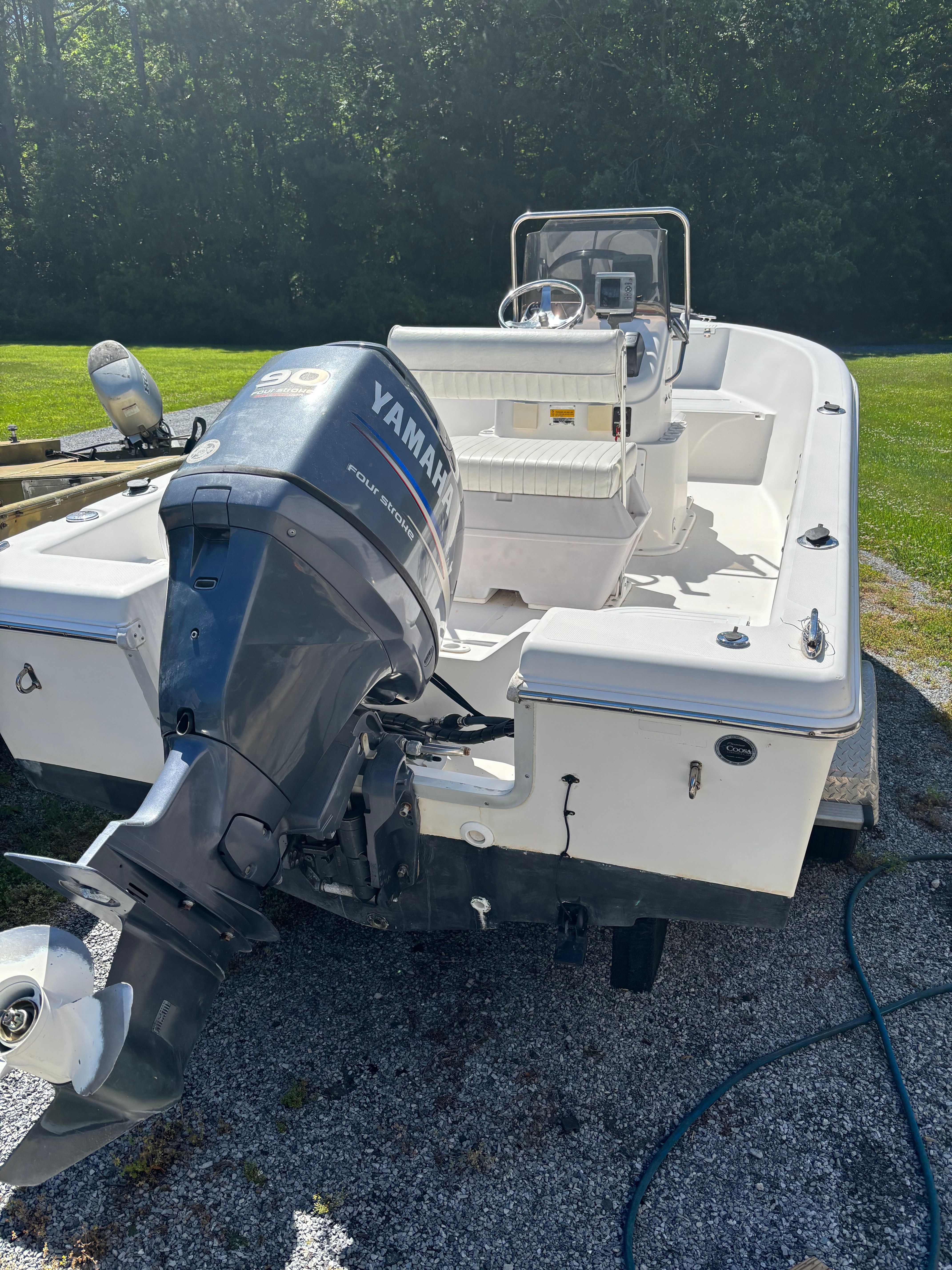 A white boat with a Yamaha outboard motor is on a gravel path next to a lawn.