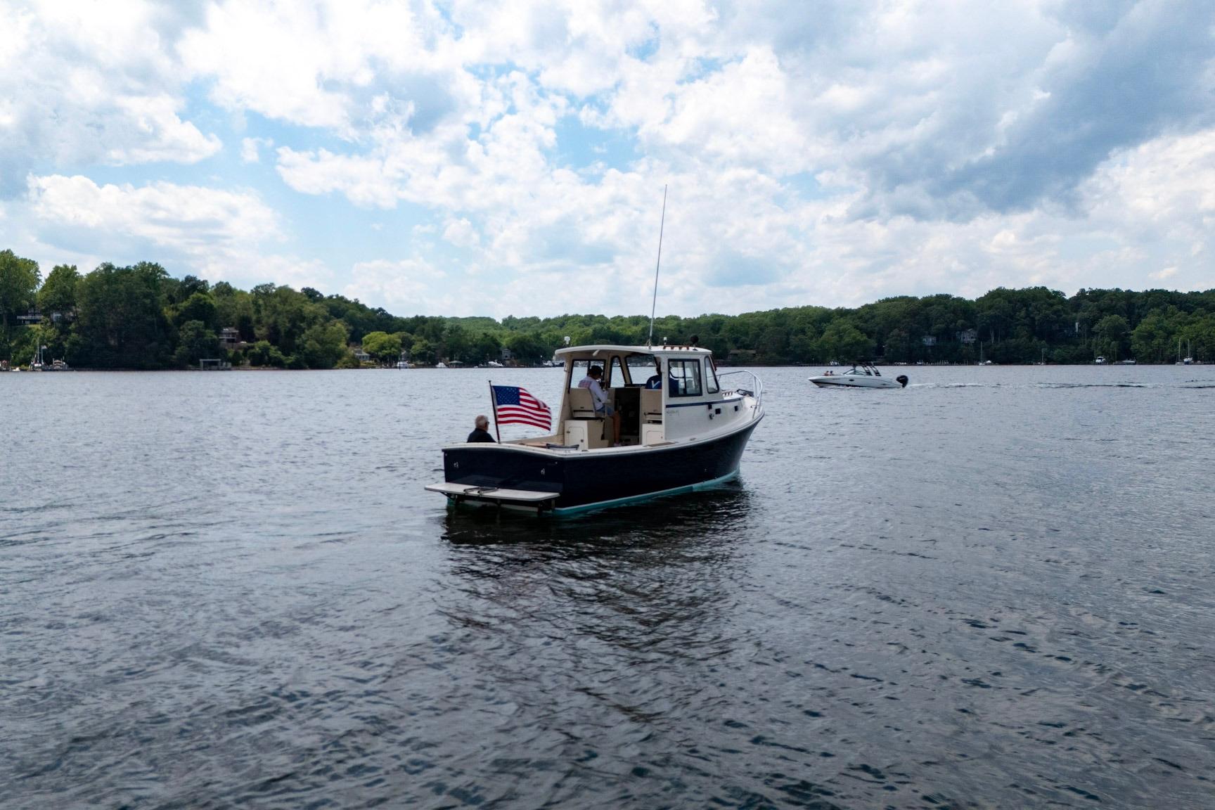 2006 Atlas Boat Works Acadia 25 on a serene lake with American flag.