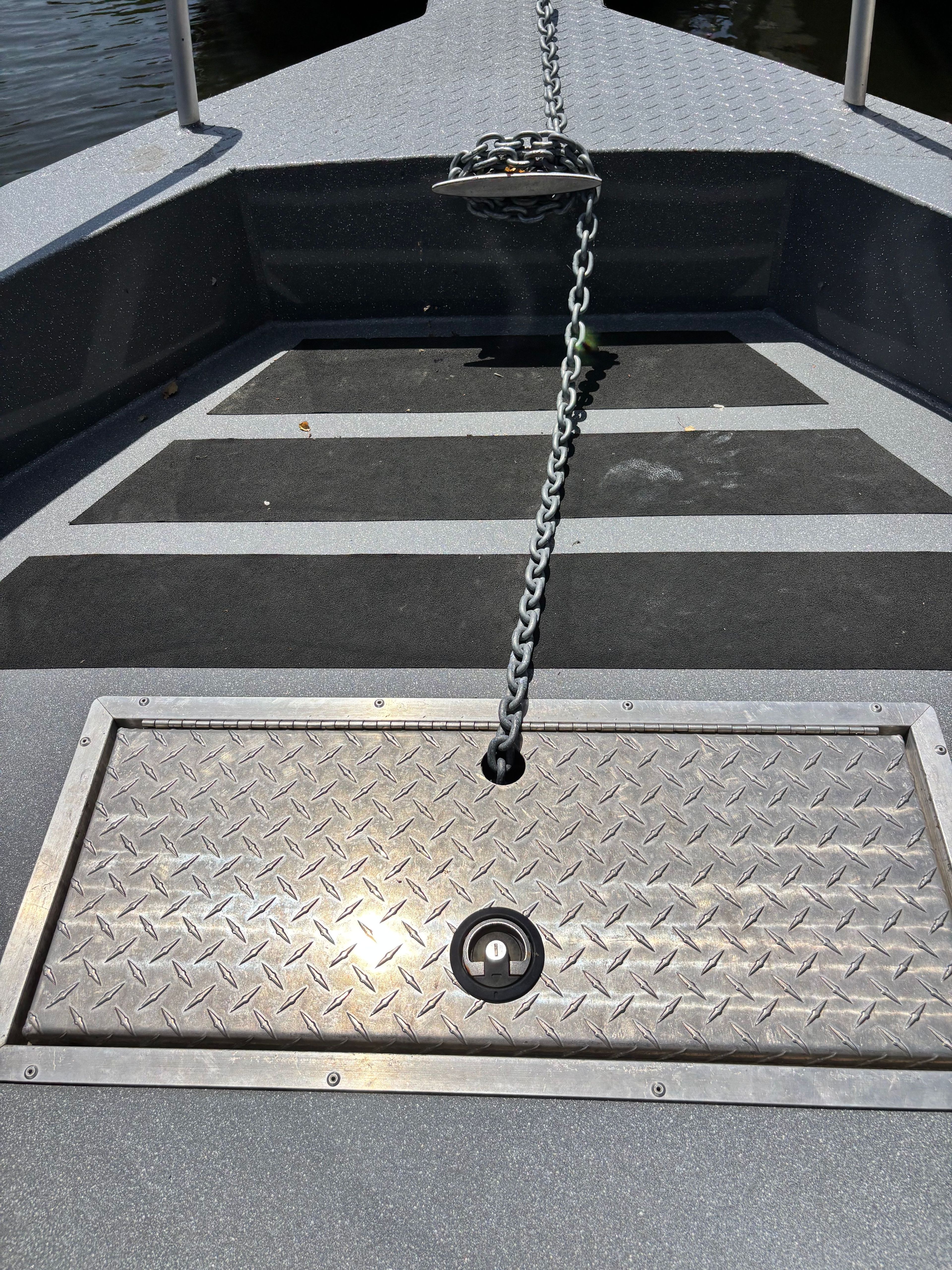Bow deck of a boat with anchor chain and storage compartment.