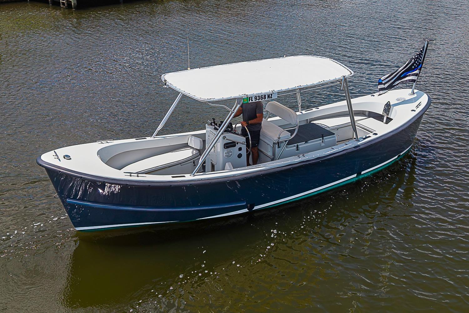 Custom 1969 boat with canopy cruising on calm water, displaying a flag at the stern.