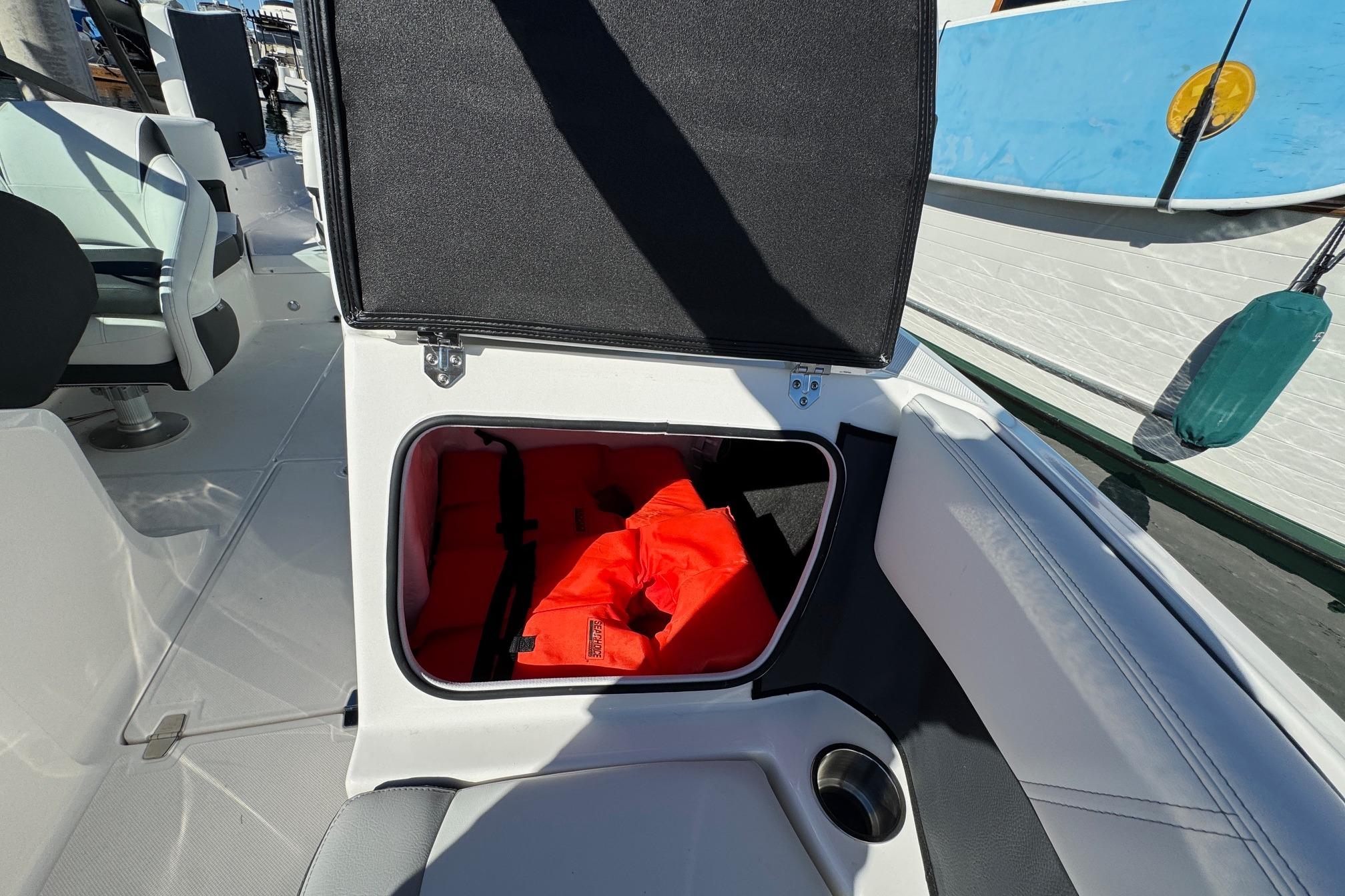 Open storage compartment on 2026 Regal 21 OBX boat with life jackets inside.