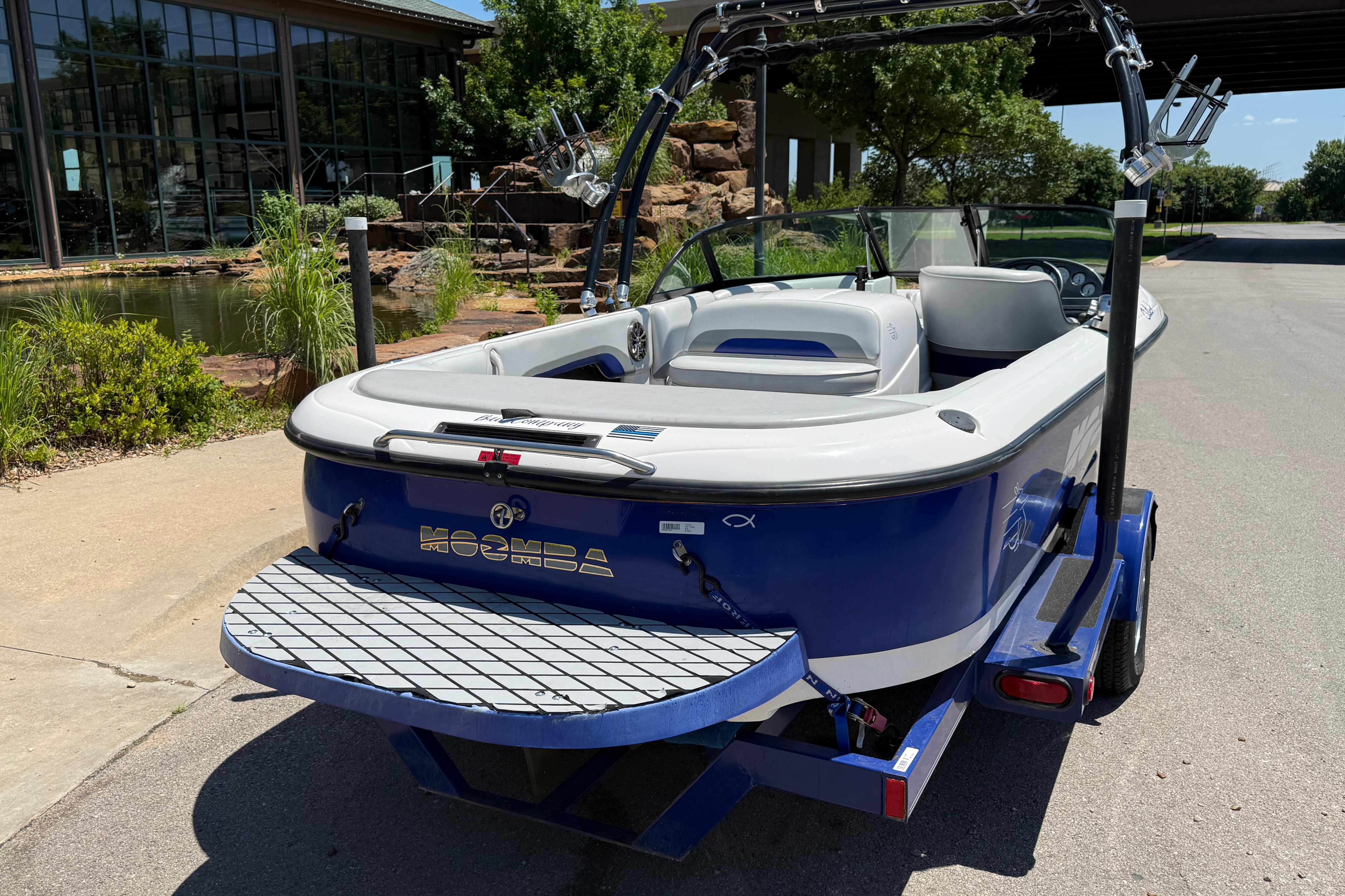 2001 Moomba Outback boat in blue, parked near a pond with lush greenery.