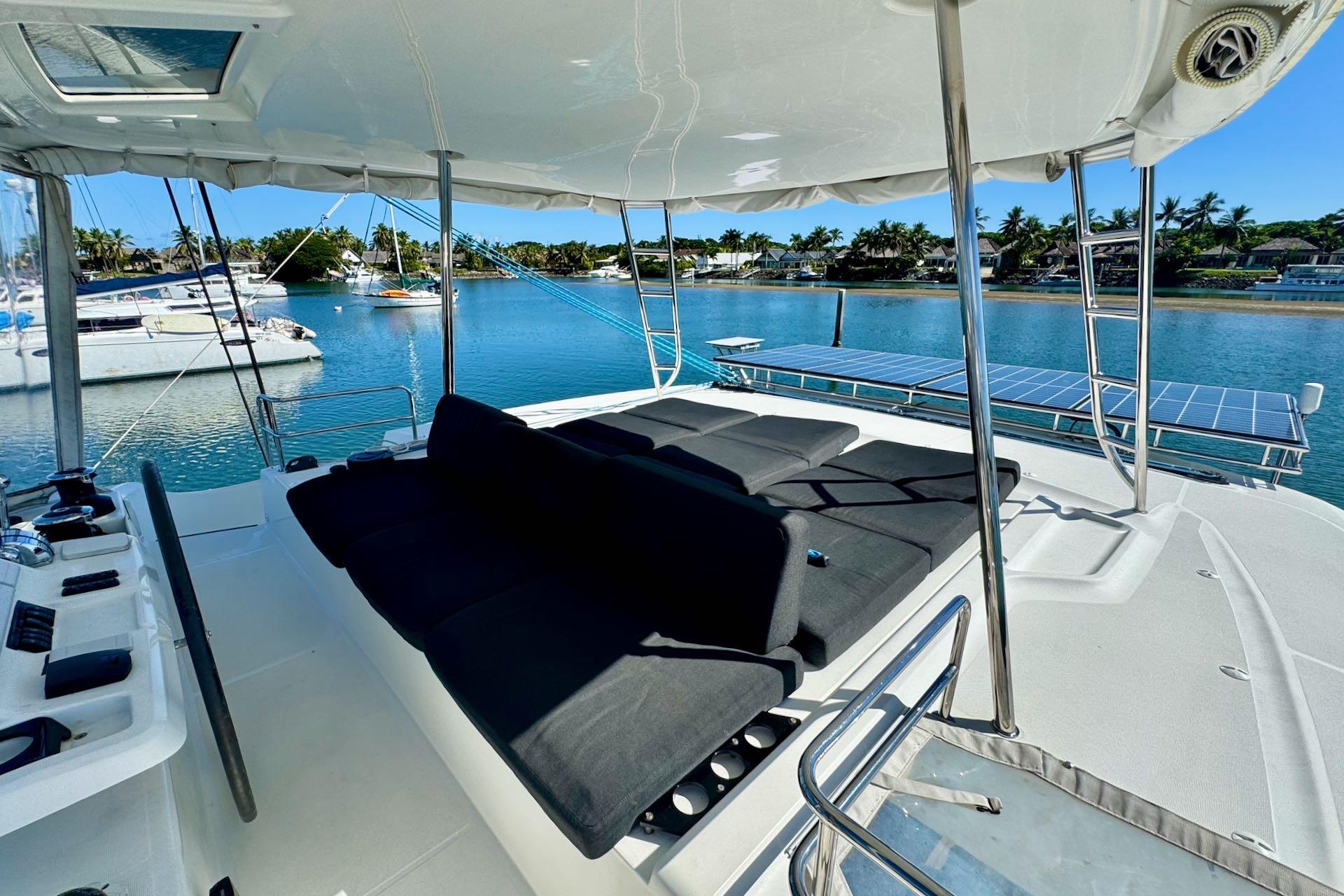 Flybridge view of 2018 Lagoon 50 catamaran with sun loungers and scenic marina backdrop.