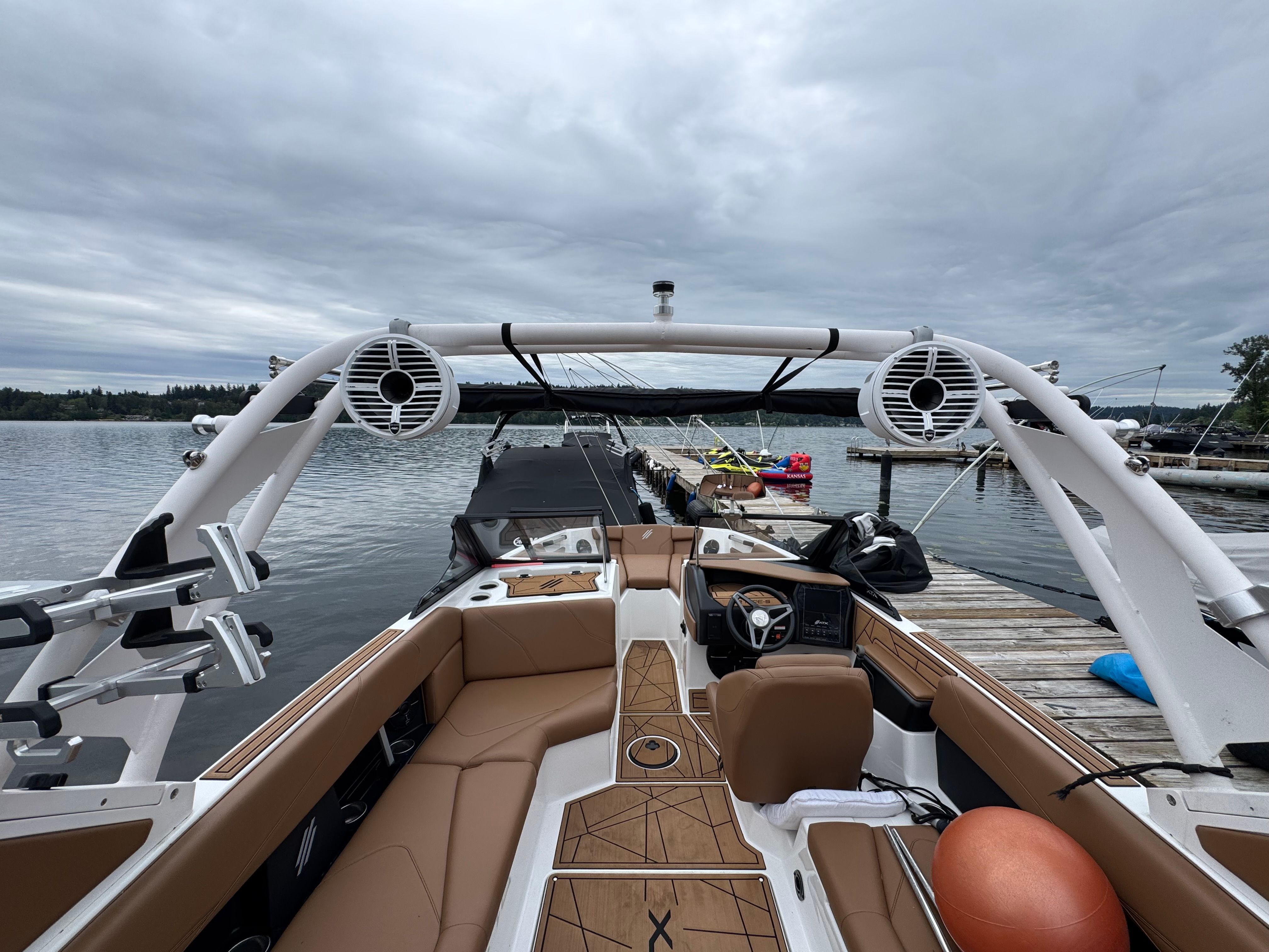A 2022 ATX Surf Boat 22 Type-S docked. It features brown seating and large speakers.