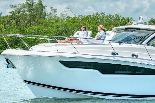 2025 Pursuit OS 405 yacht with two people relaxing on deck, surrounded by lush greenery.