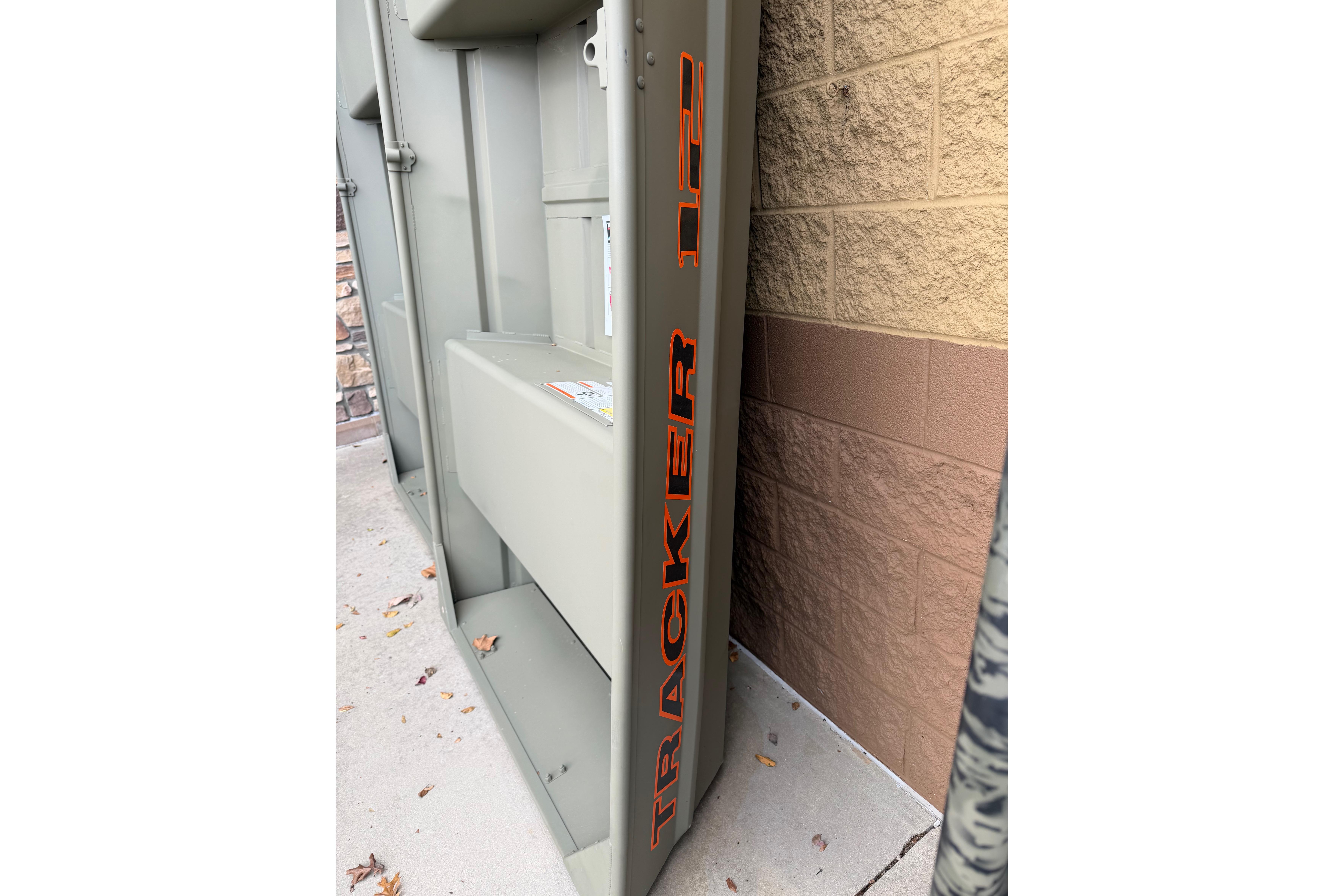 2026 Tracker Grizzly 12 Jon boat, side view with orange lettering, against brick wall.