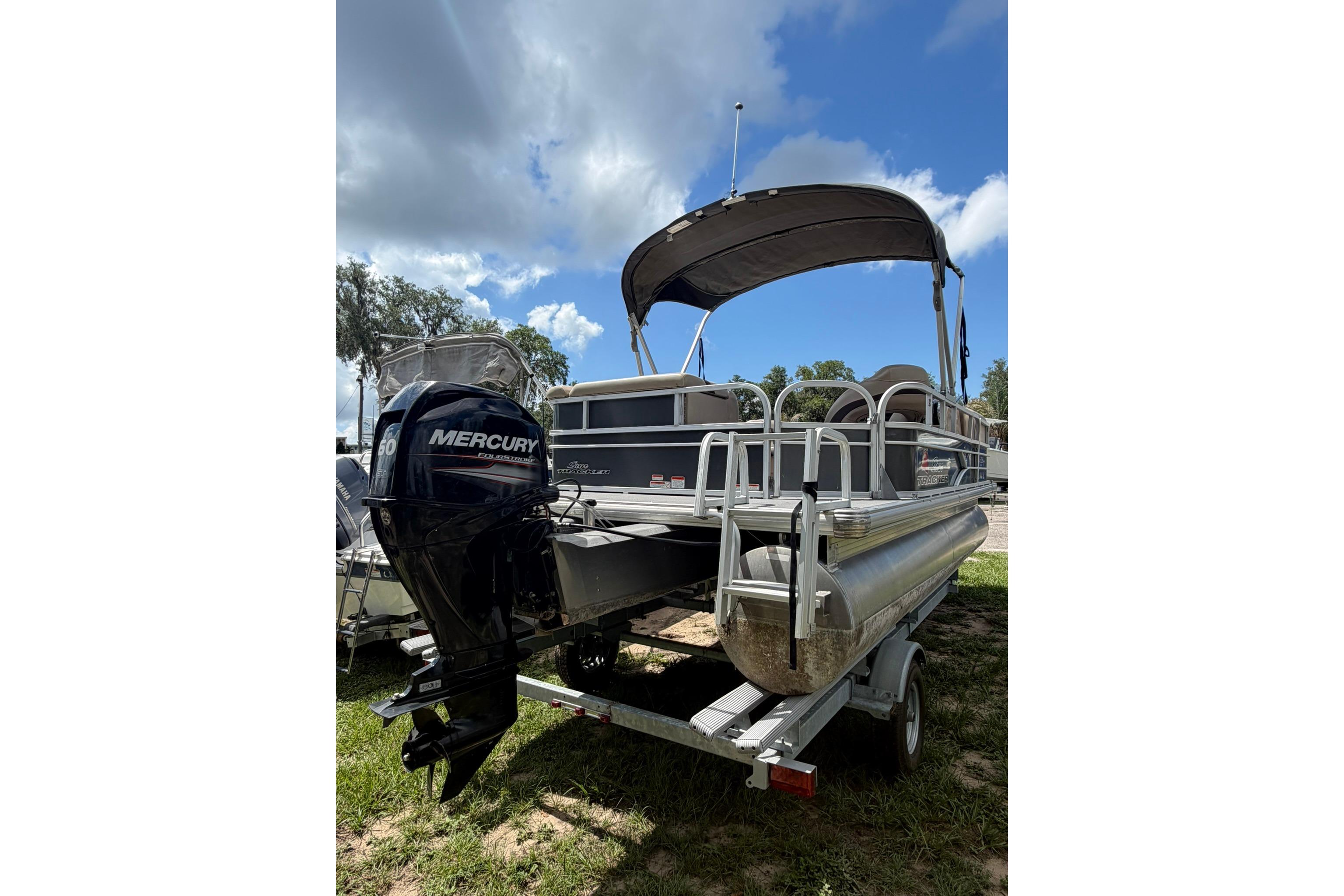 2016 SUNTRACKER Party Barge 20 pontoon boat with Mercury outboard motor, parked on grass.