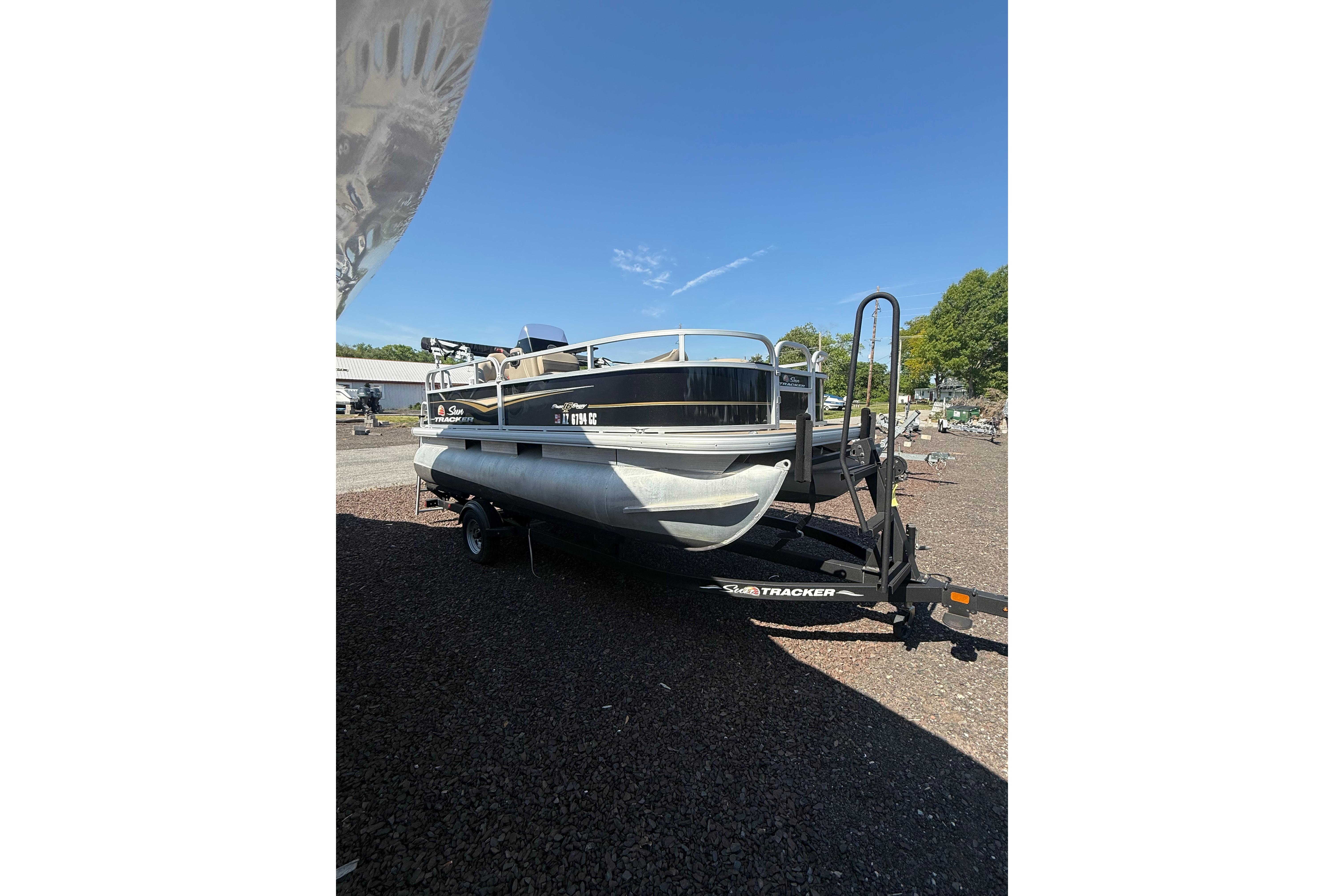 2021 Sun Tracker Bass Buggy 16 XL Select pontoon boat on trailer, parked outdoors.