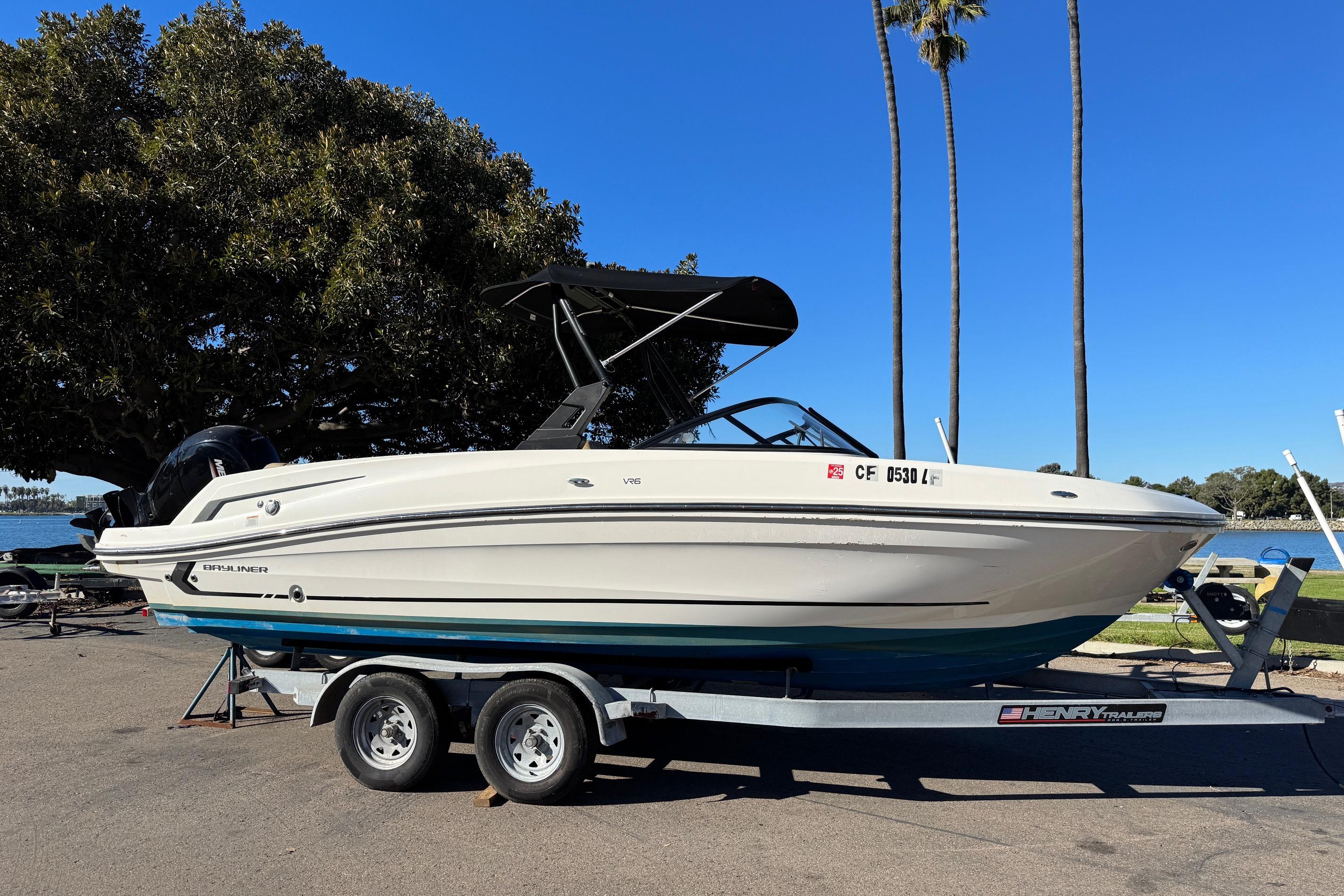 2022 Bayliner VR6 Bowrider OB on trailer, parked near a lake with trees.