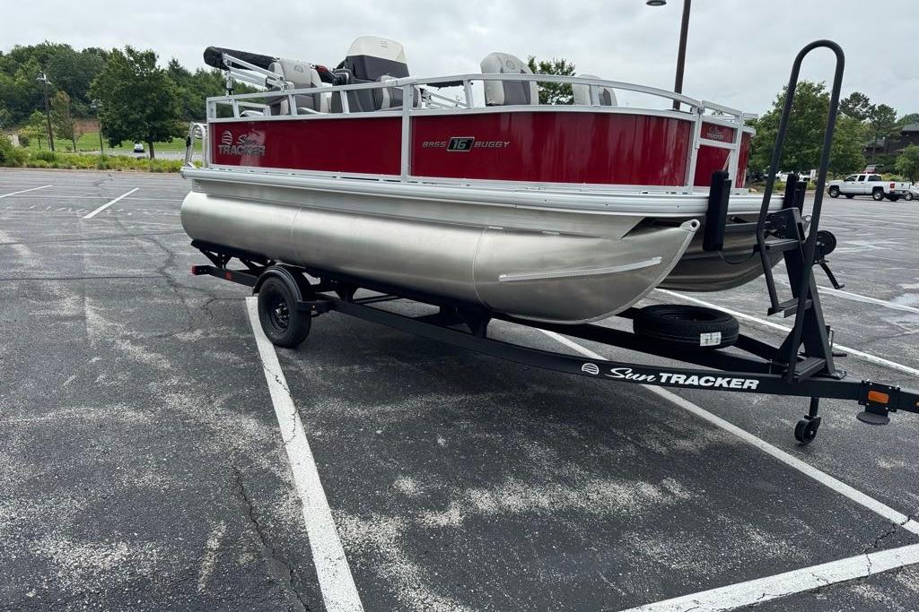 2026 Sun Tracker Bass Buggy 16 XL Select pontoon boat on trailer in parking lot.