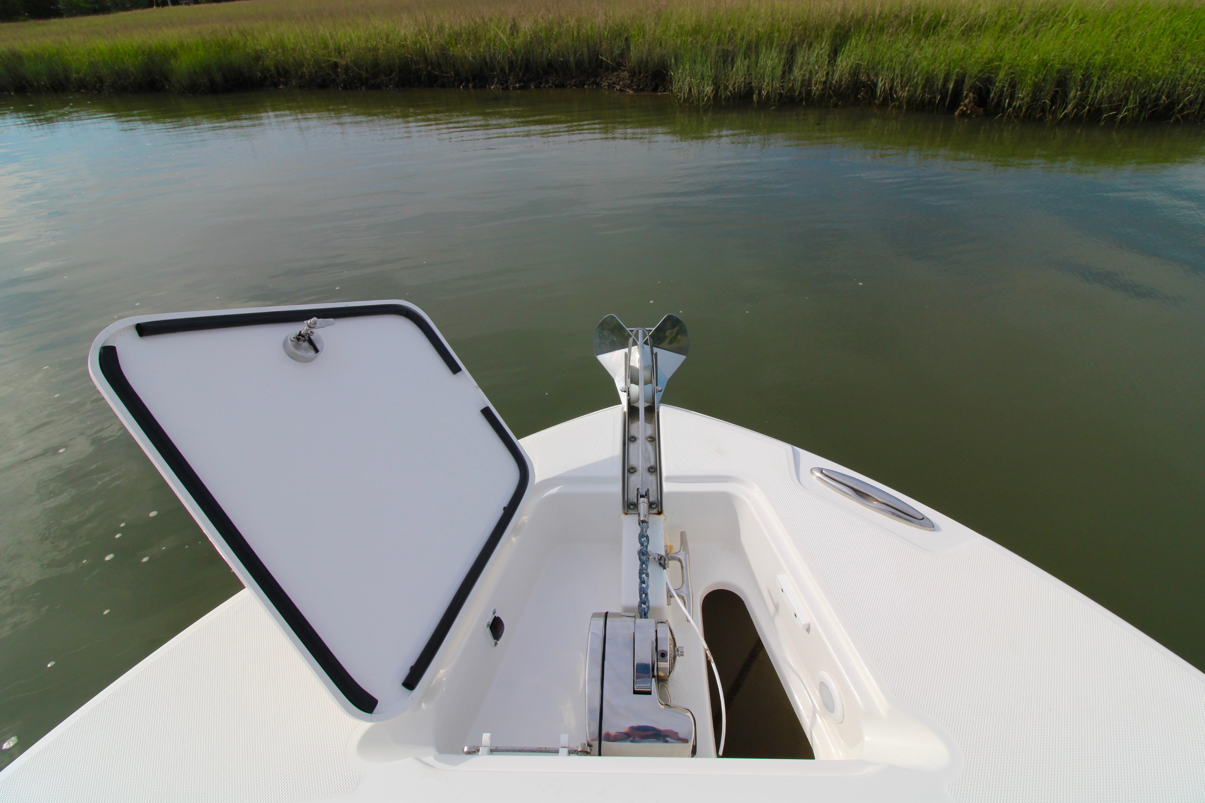 Open anchor compartment on 2022 Edgewater 280CC boat, near calm water and grassy shoreline.