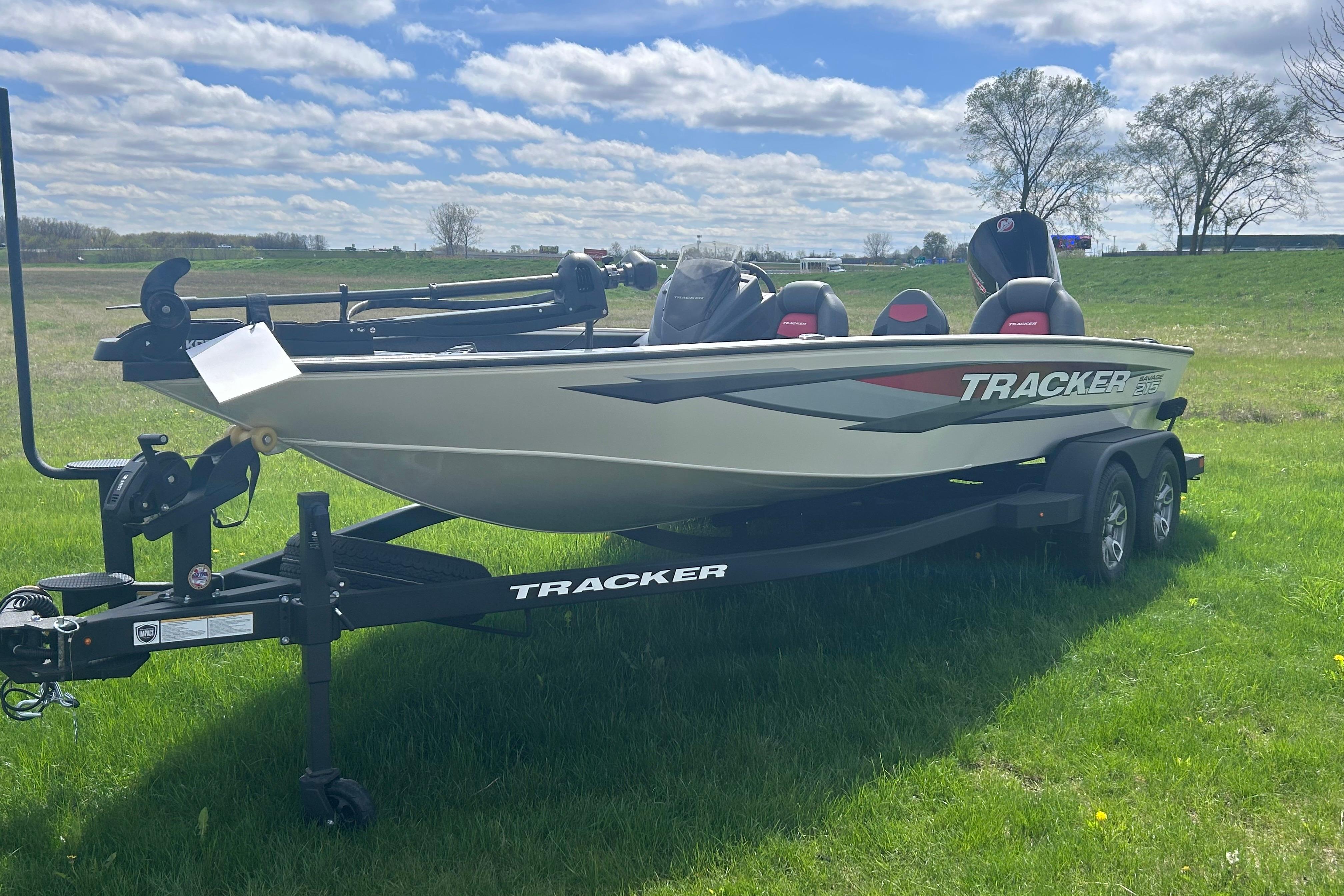 2025 Tracker Savage 215 boat on trailer in grassy field under blue sky.